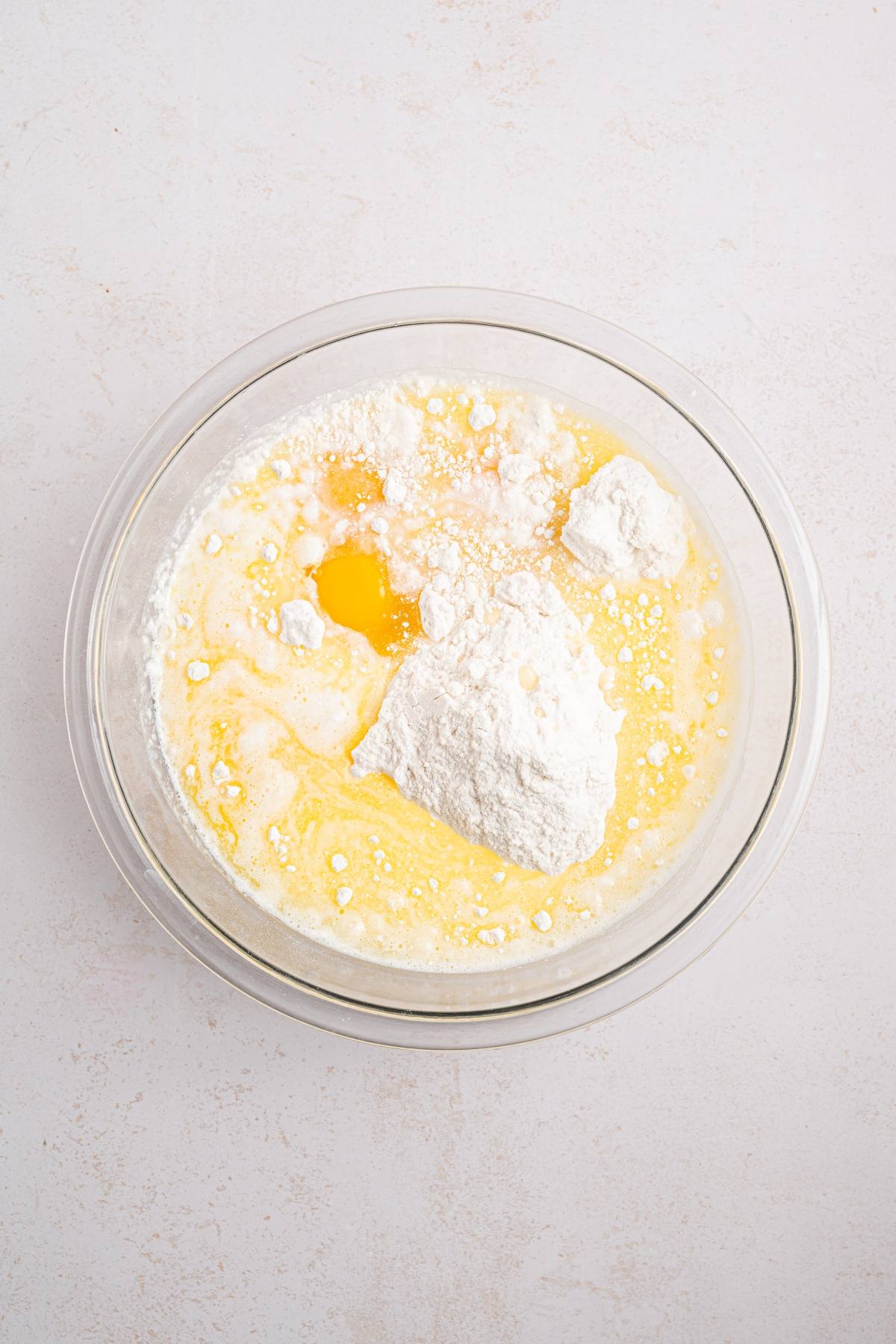 A glass bowl with flour, eggs, and wet ingredients ready to be mixed for baking.