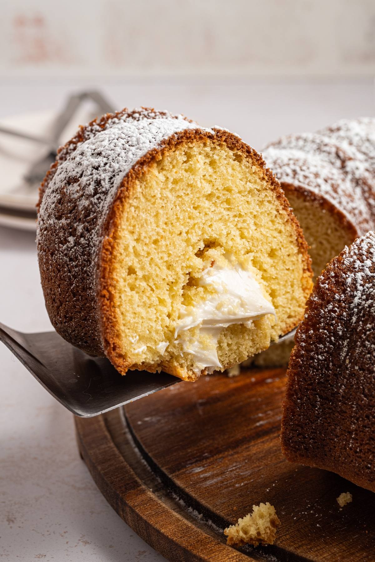 A slice of bundt cake with cream filling and powdered sugar, served on a spatula.