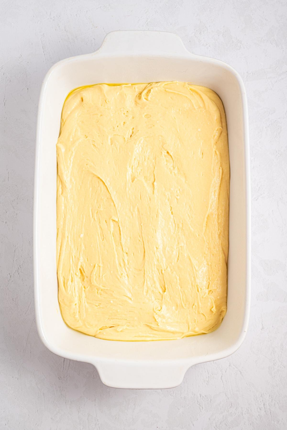 Rectangular white baking dish filled with smooth yellow cake batter on a light surface.