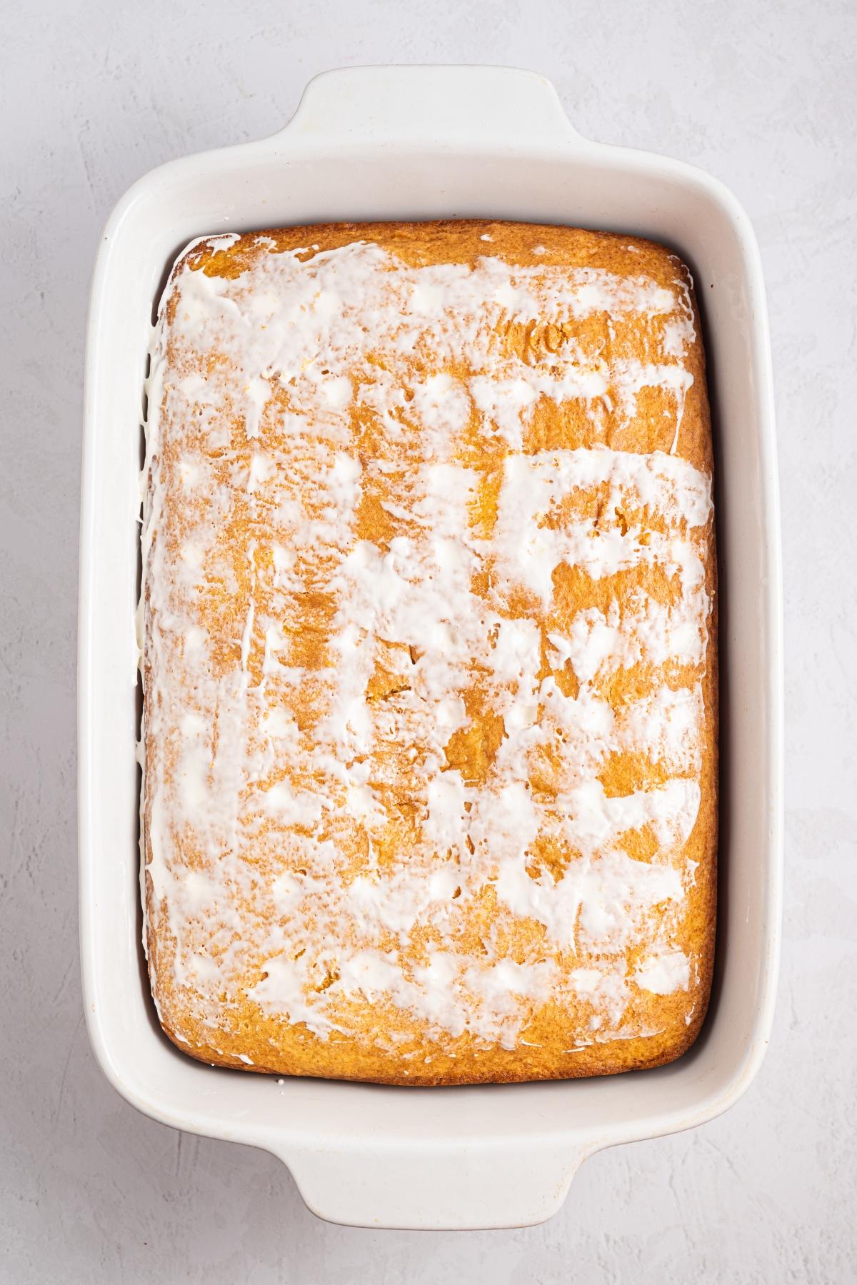 A baked cake in a white rectangular dish, topped with a thin layer of white icing.