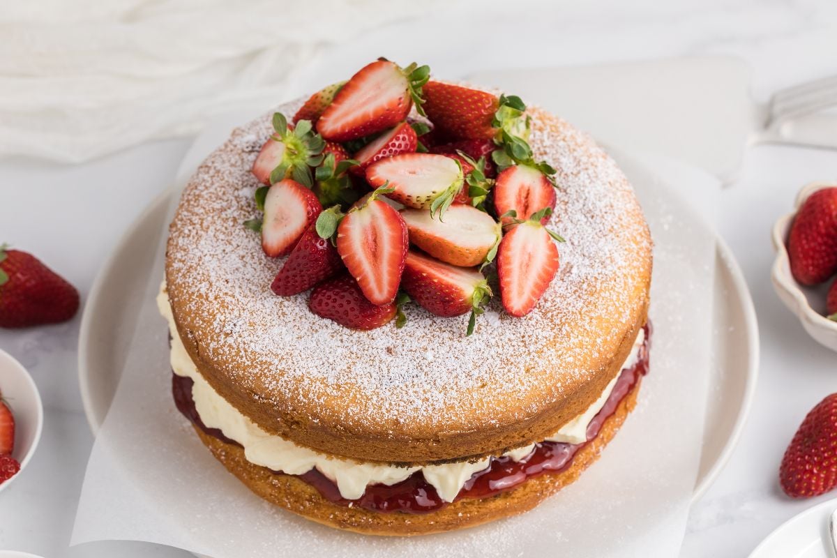 Classic Victoria Sandwich Cake: a round sponge cake filled with cream and jam, topped with halved strawberries and dusted with powdered sugar.