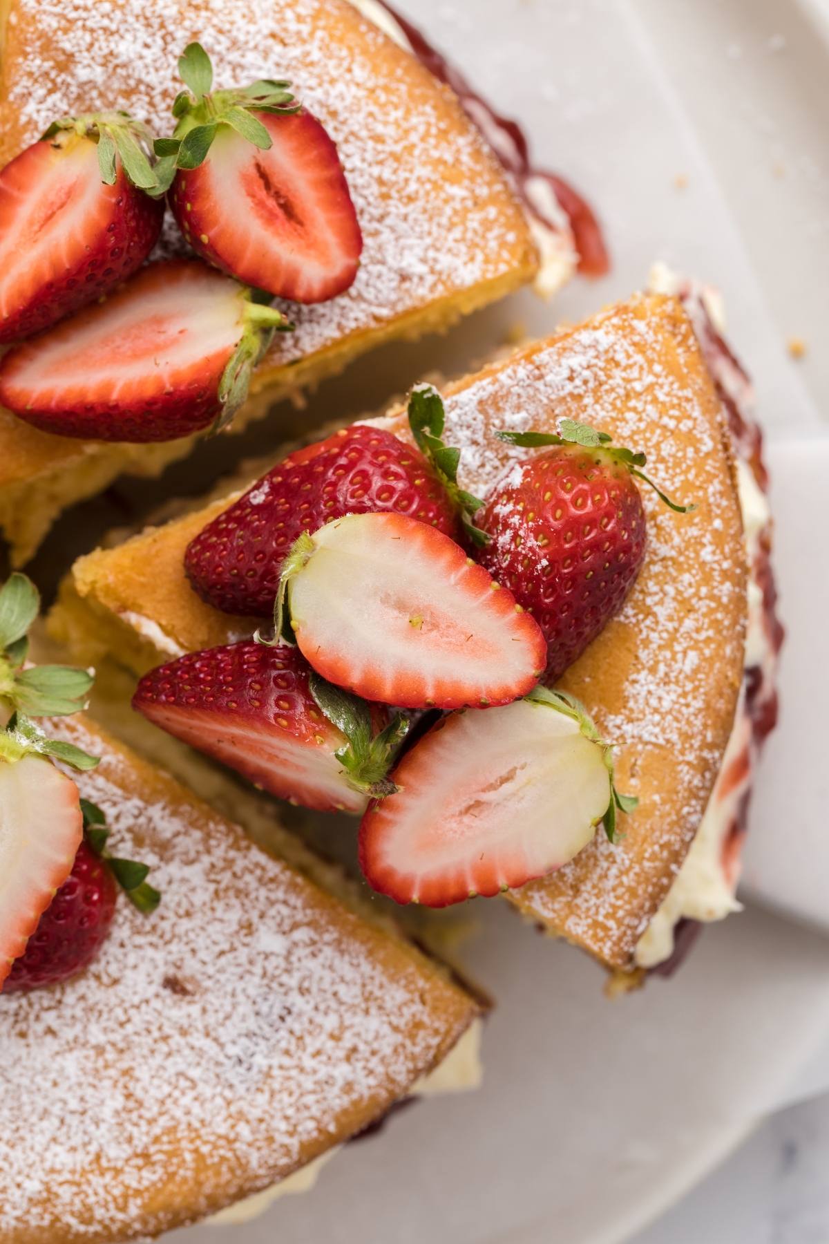 Close-up of a sliced sponge cake topped with halved strawberries and dusted with powdered sugar.