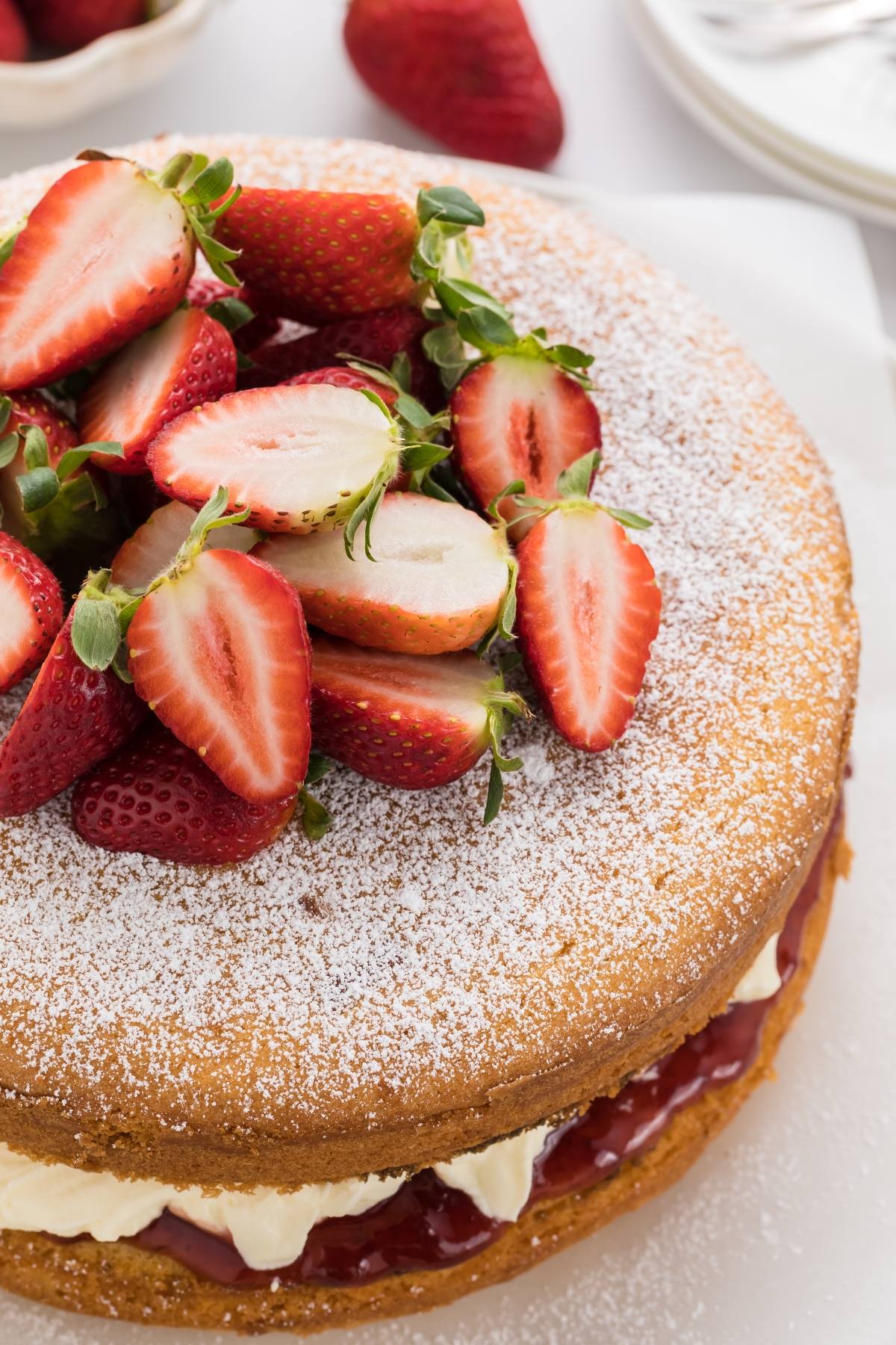 A sponge cake with cream and jam filling, topped with halved strawberries and dusted with powdered sugar.