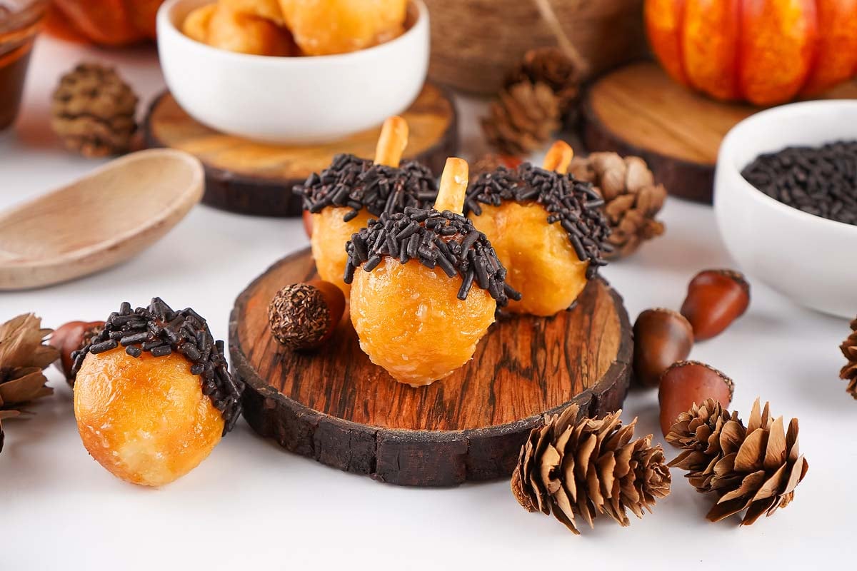 Small acorn donut holes with chocolate sprinkles, surrounded by pinecones and autumn decor.