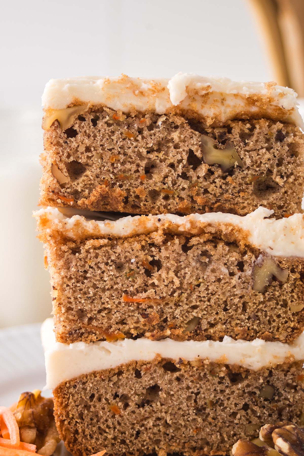 Close-up of three stacked carrot cake bars with cream cheese frosting and visible pecan pieces.