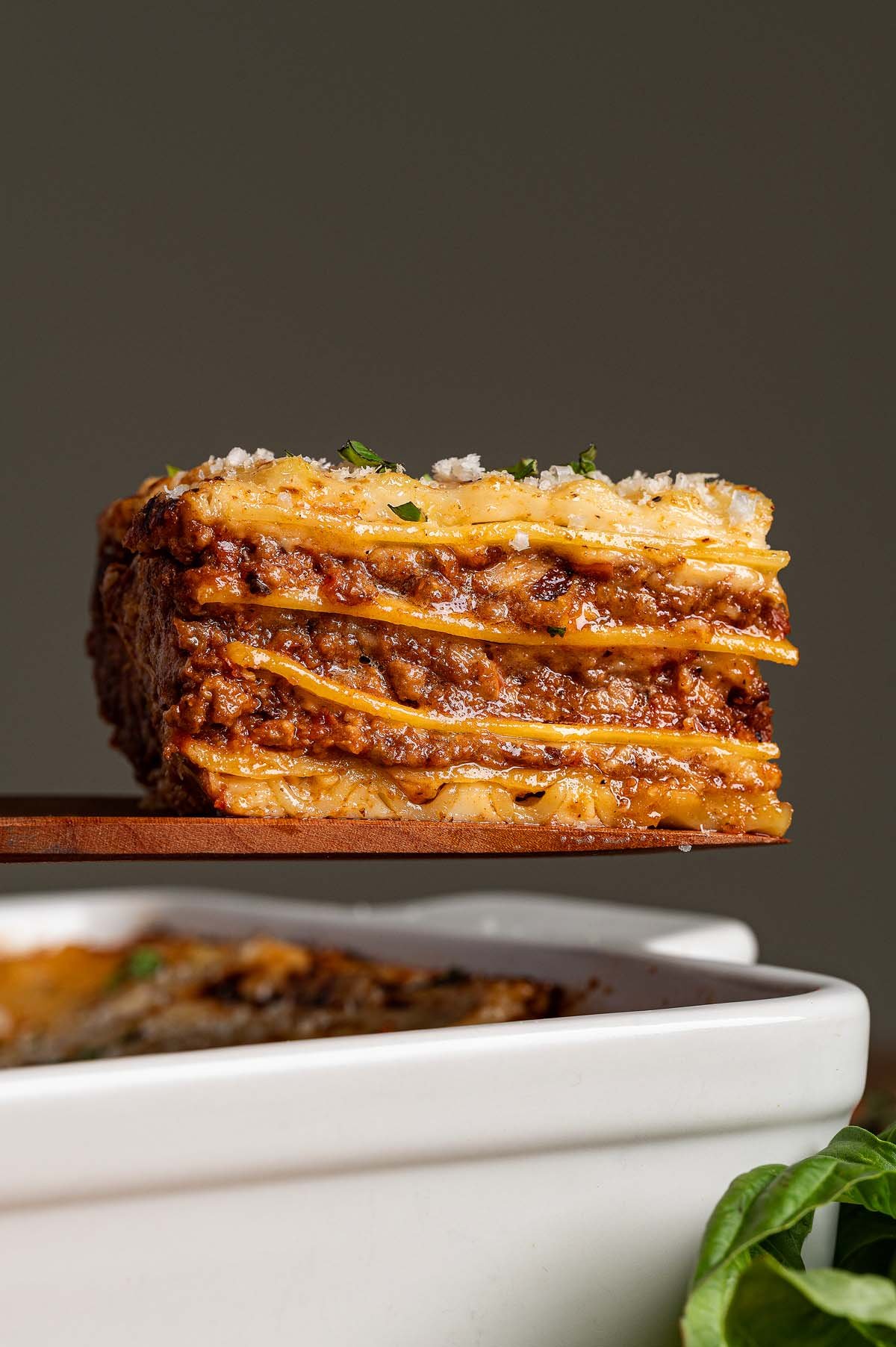 A close-up of a slice of lasagna alla Bolognese with layers of pasta, meat sauce, and cheese, held above a white dish.