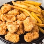 A black plate with crispy popcorn chicken and golden French fries sits beside a striped napkin.