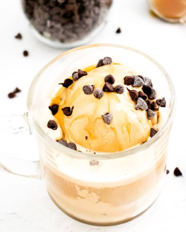 A glass mug of coffee with a scoop of ice cream, chocolate chips, and caramel drizzle on top—a delightful treat inspired by Italian dessert recipes.