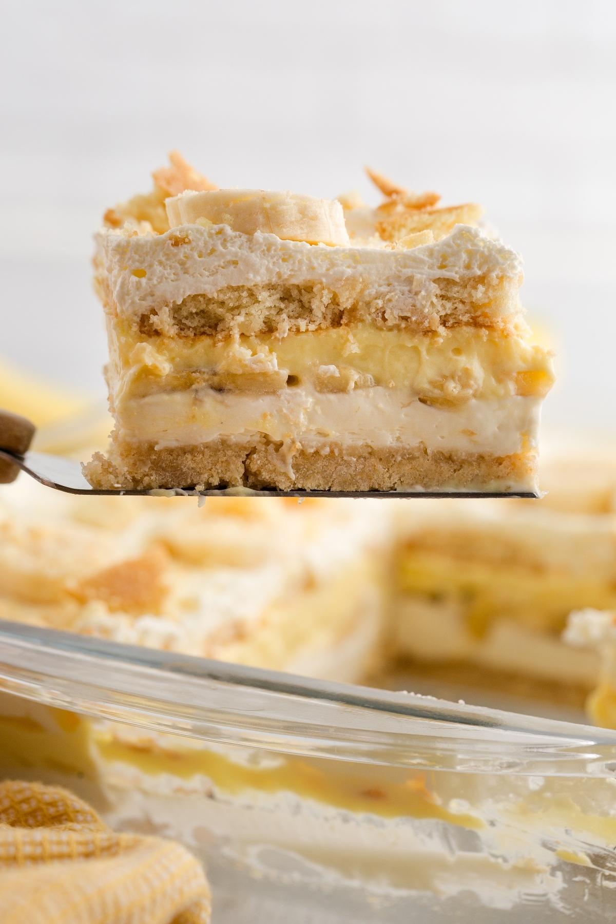 A close-up of a slice of creamy banana pudding layered dessert being lifted from a glass dish.