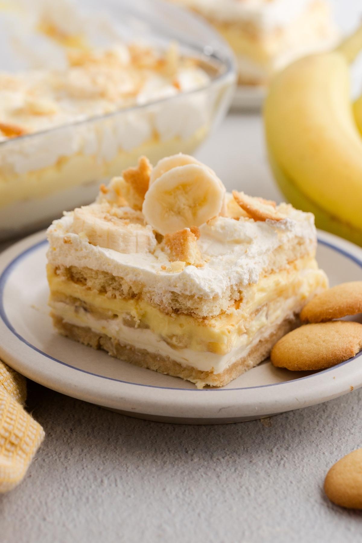 A slice of banana pudding dessert with layers, topped with banana and cookie crumbs on a plate.