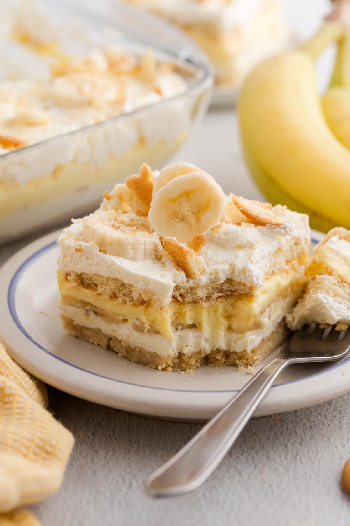 A slice of banana pudding dessert with whipped cream and banana slices on a plate, next to a fork.