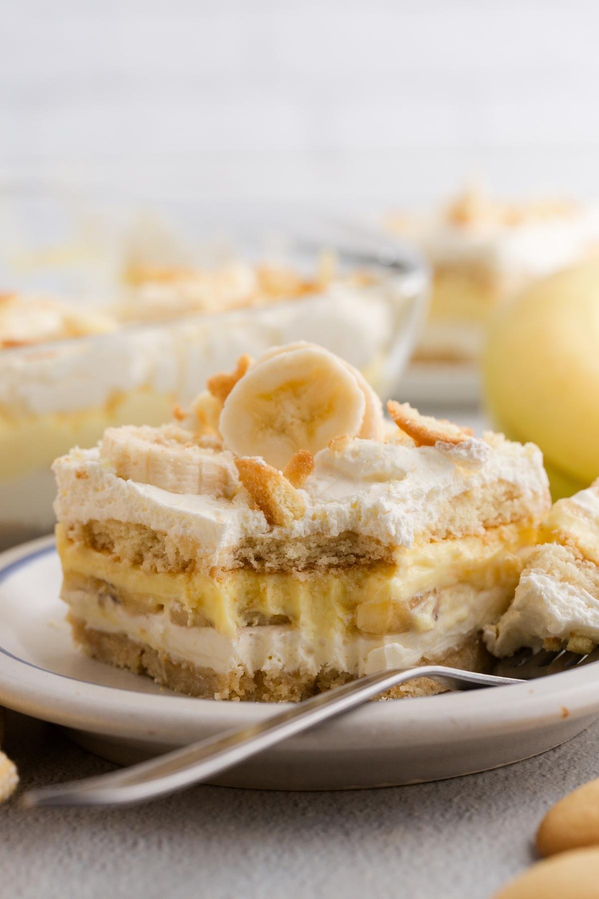 A slice of banana pudding dessert topped with whipped cream and banana slices on a plate with a fork.