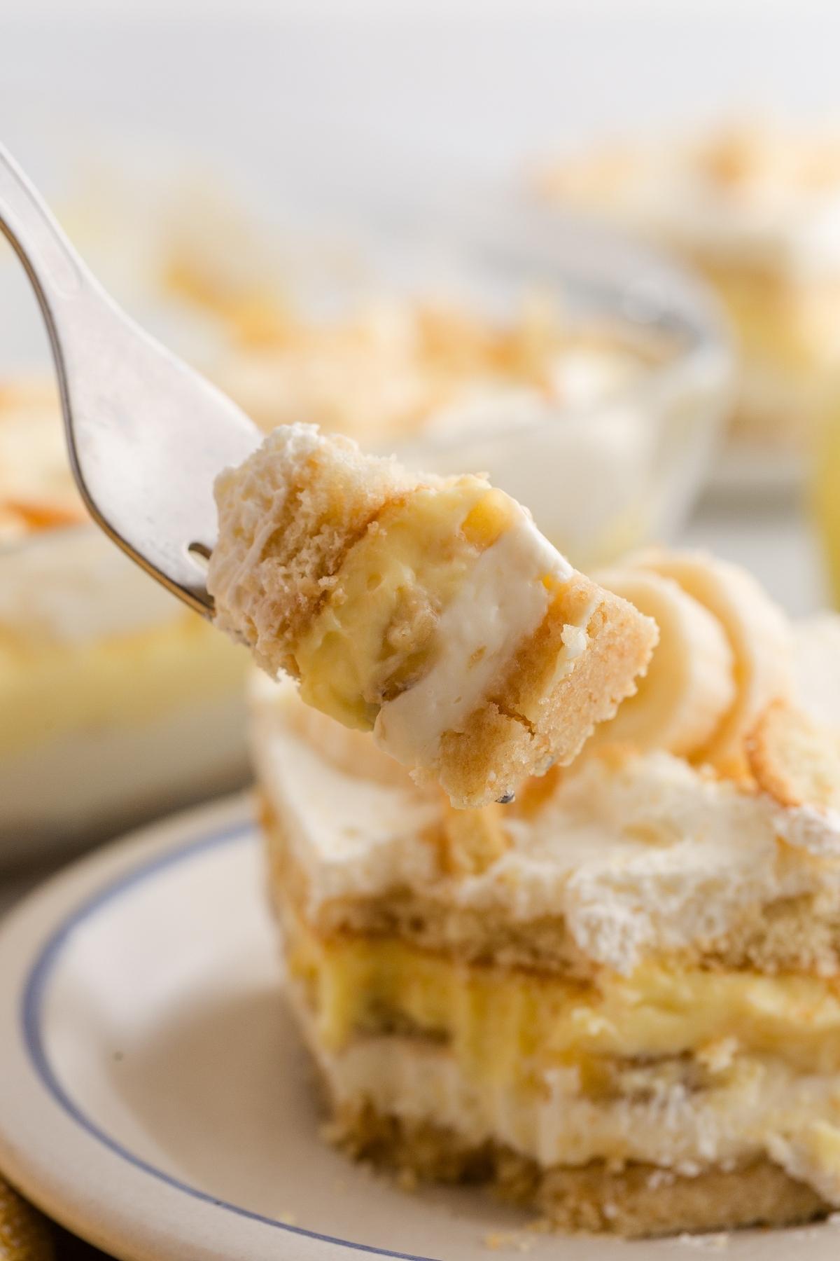 A fork holds a bite of creamy layered banana pudding dessert above a plate with a larger serving.