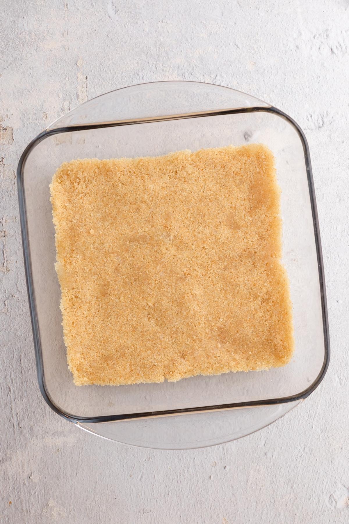 Glass dish with an even layer of crumbly, light brown crust pressed into the bottom.