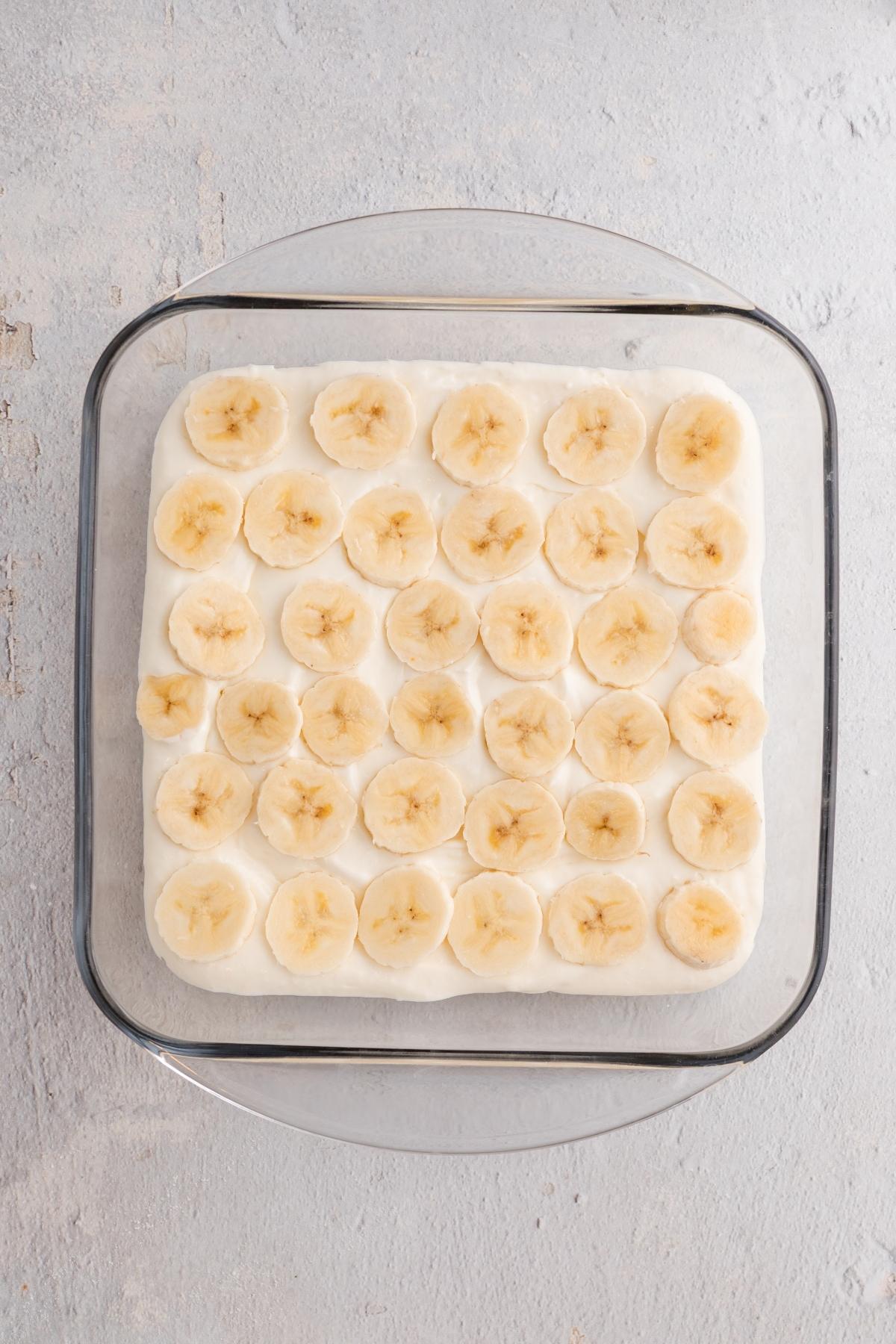 Glass dish with a layer of banana slices on top of a creamy white dessert, viewed from above.