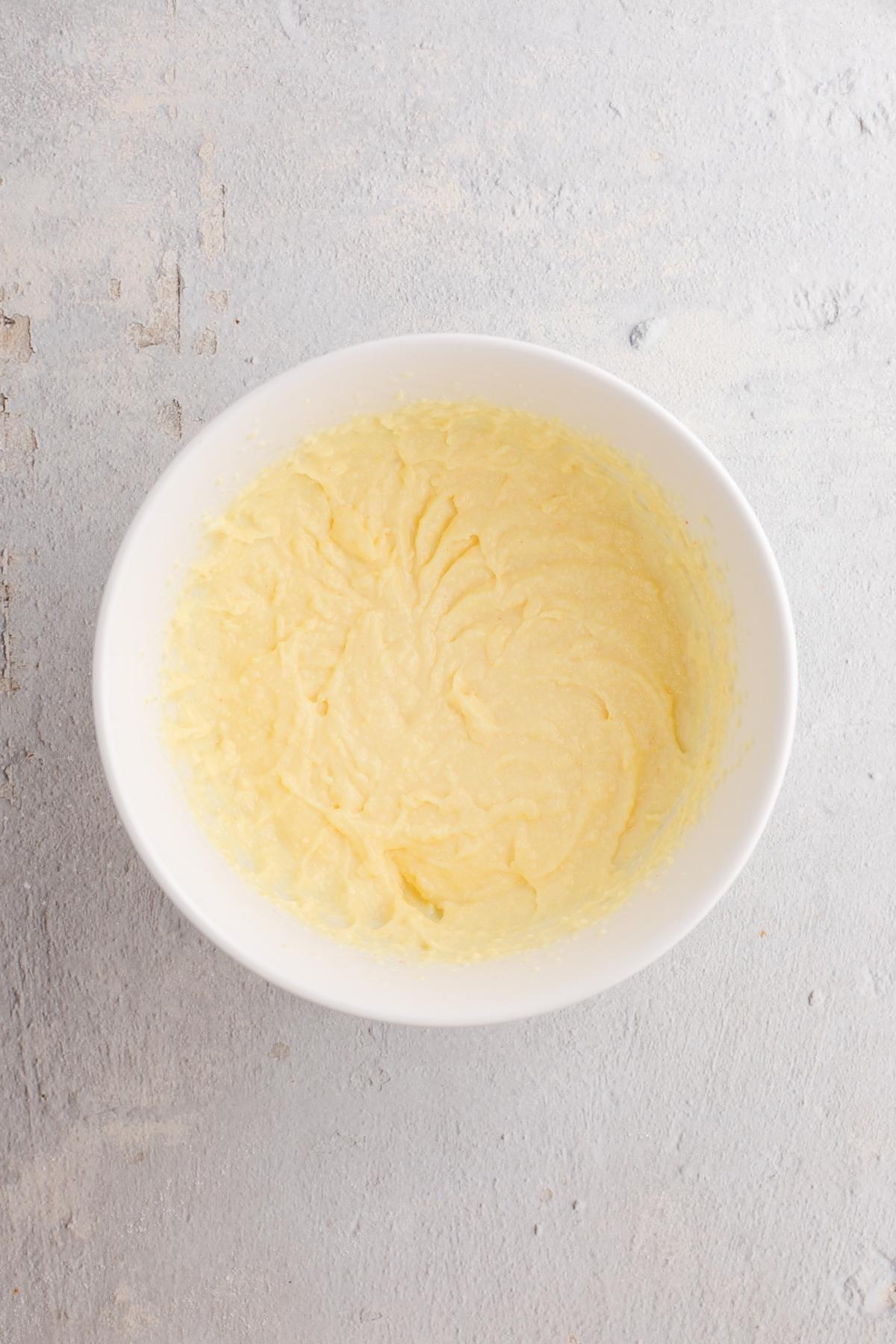 A white bowl filled with creamy yellow cake batter on a light gray textured surface.