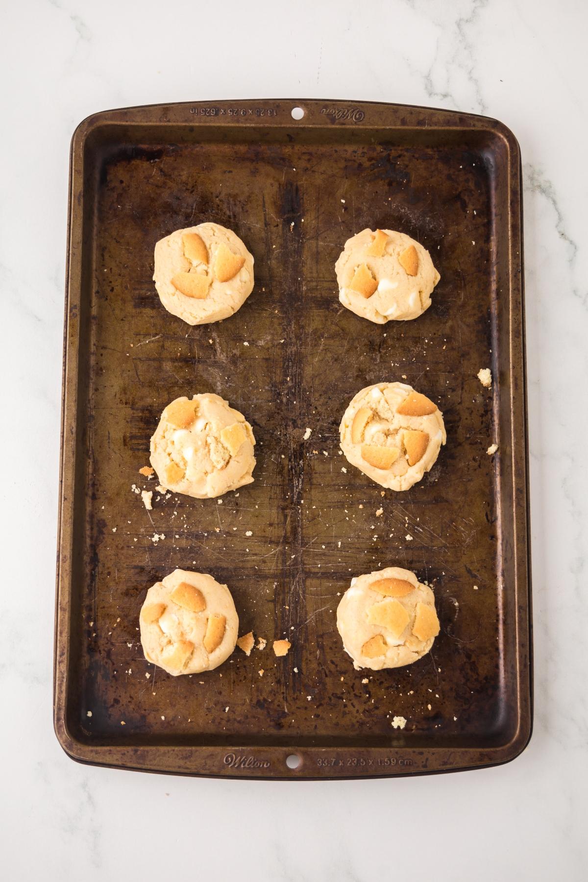 A baking sheet with six round cookies spaced apart, on a white marble surface.
