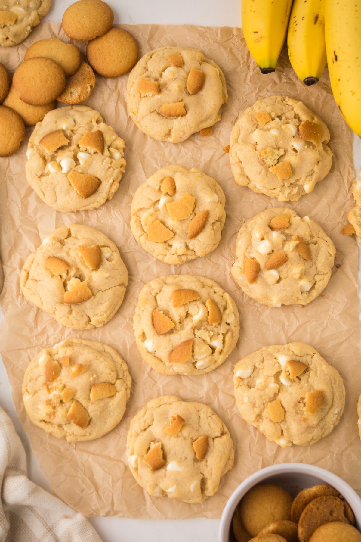 Banana pudding cookies with vanilla wafers on parchment paper, surrounded by fresh bananas and cookies.