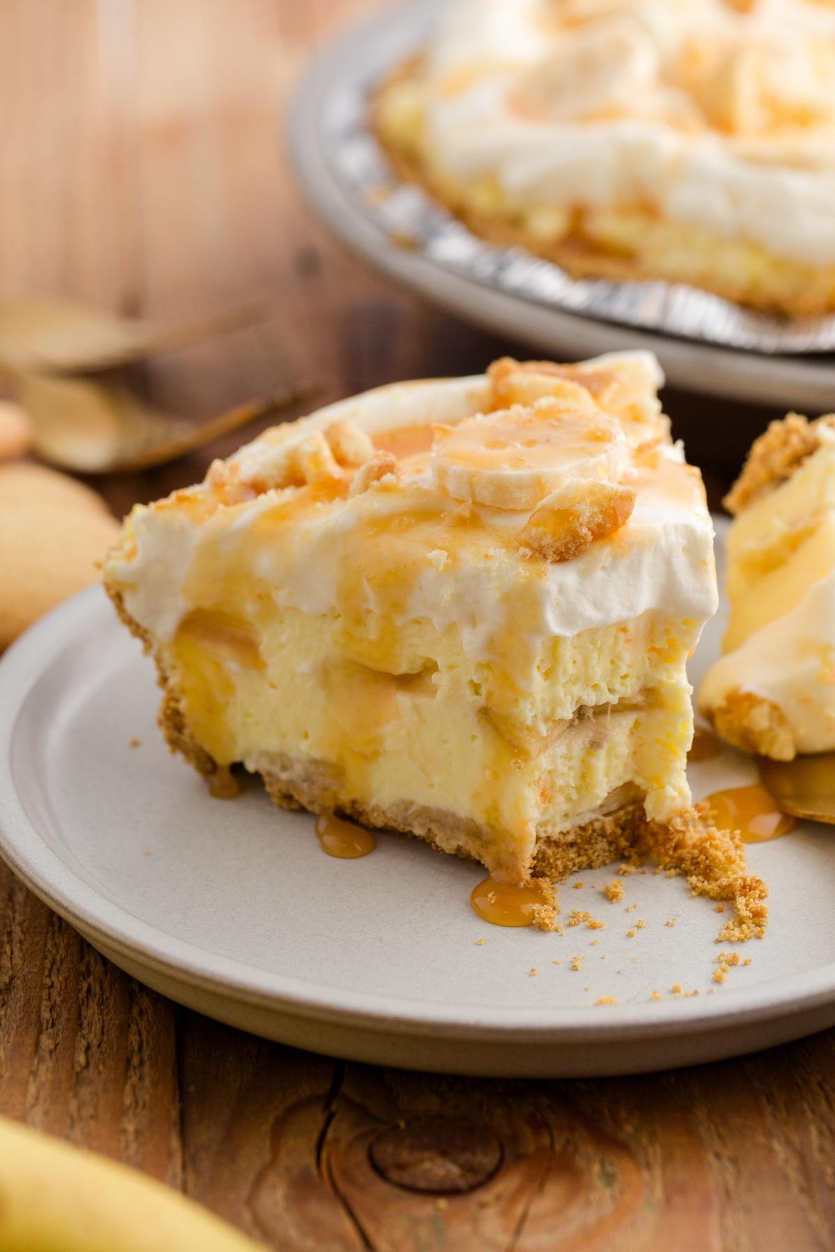 A slice of creamy banana pie with whipped topping and caramel drizzle on a plate.