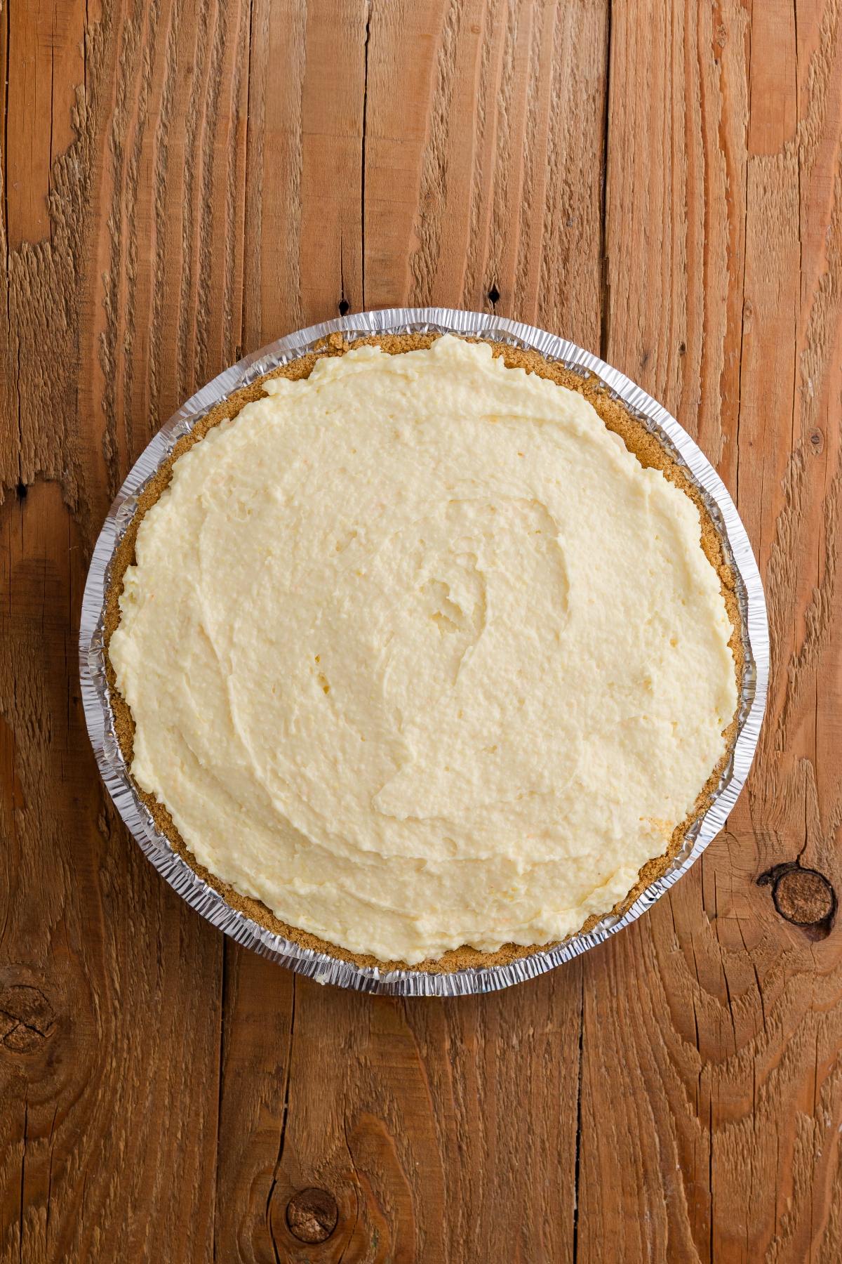 A whole cream pie in a foil tin sits on a rustic wooden surface, photographed from above.