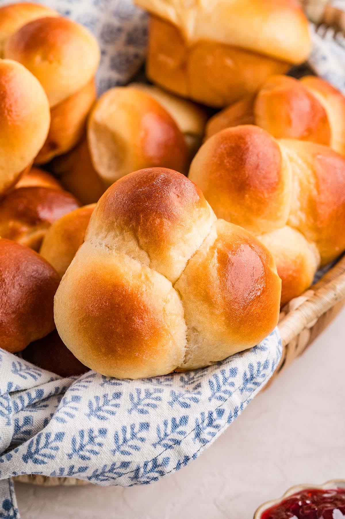 A basket of golden-brown cloverleaf rolls rests on a blue and white patterned cloth, ready to be enjoyed.