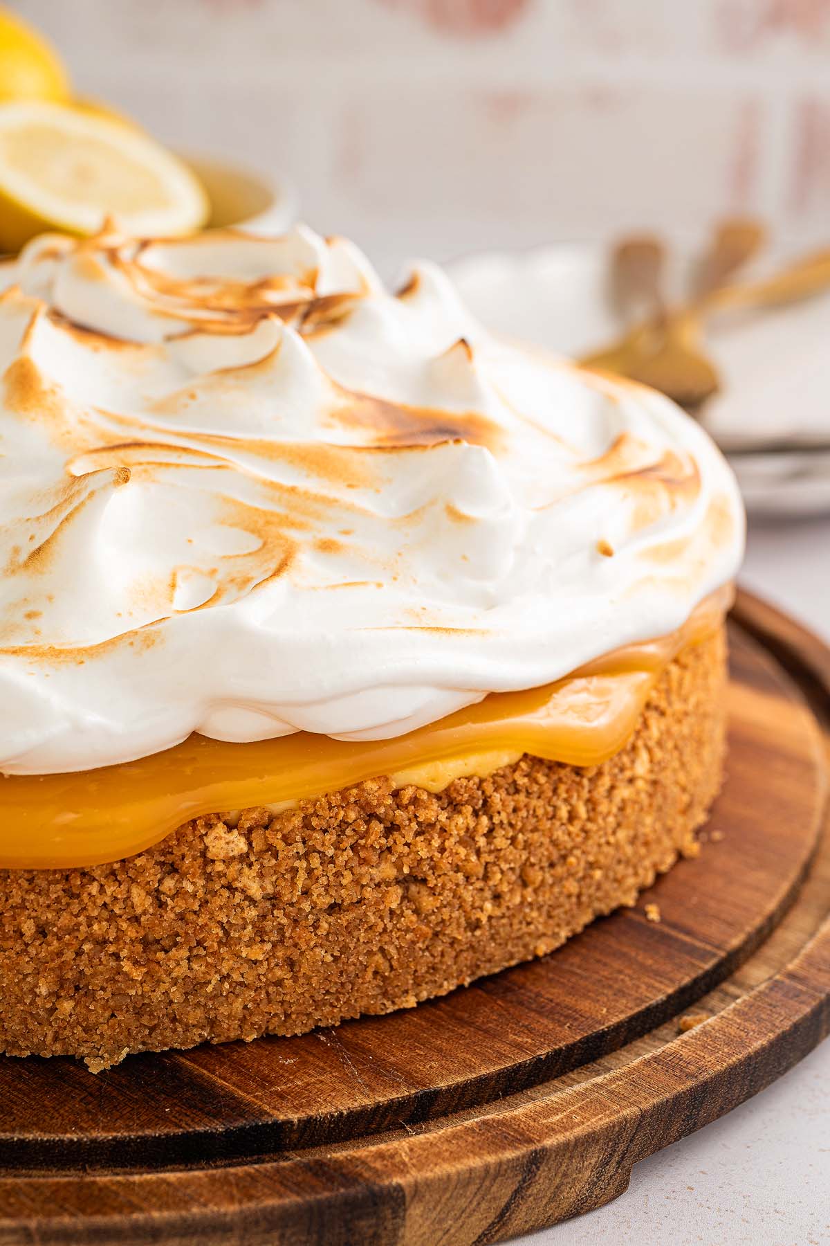 A close-up of a Lemon Meringue Cheesecake with a graham cracker crust on a wooden board.