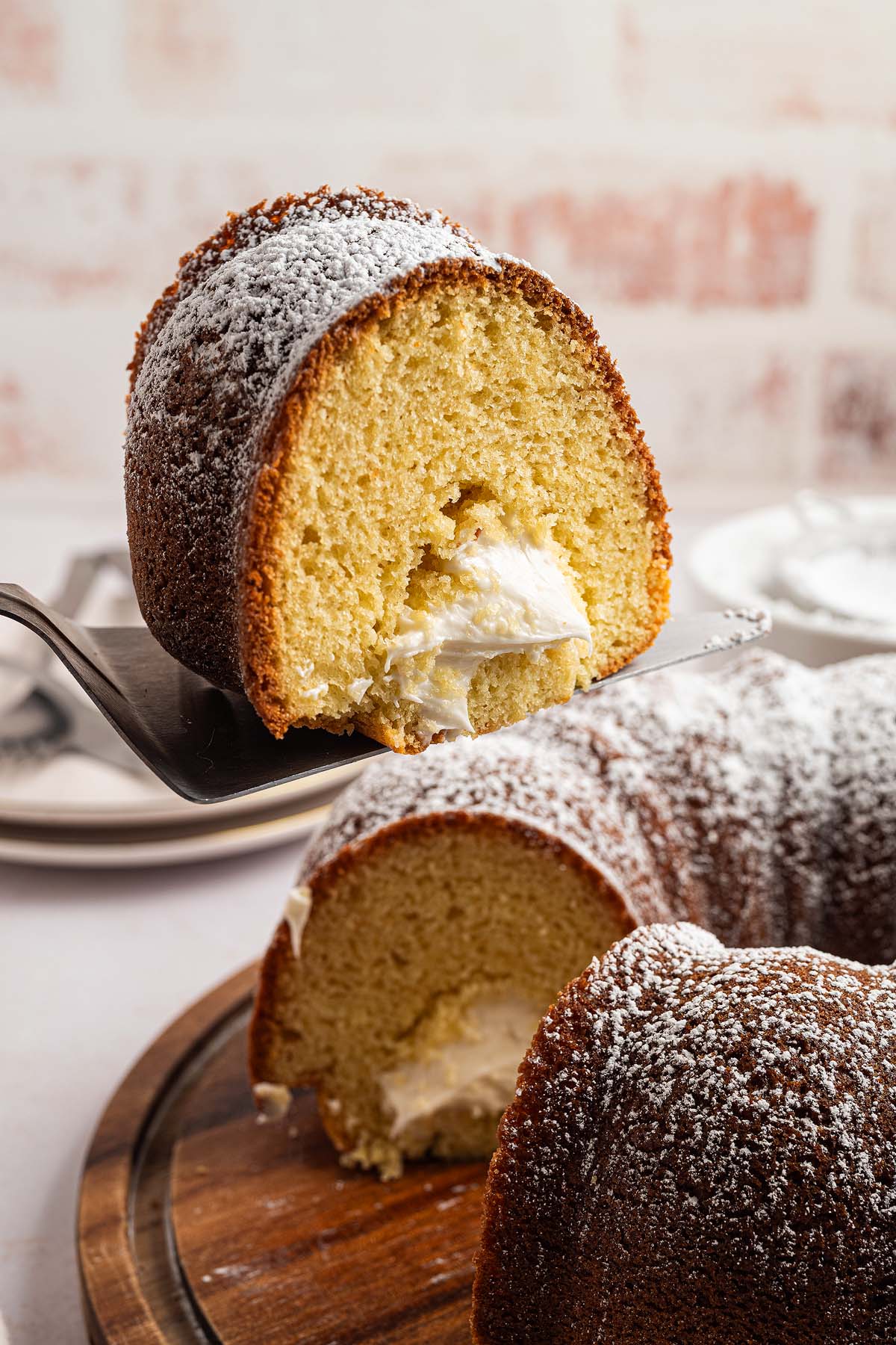 A slice of cream-filled Twinkie Cake bundt, dusted with powdered sugar, is served on a spatula.