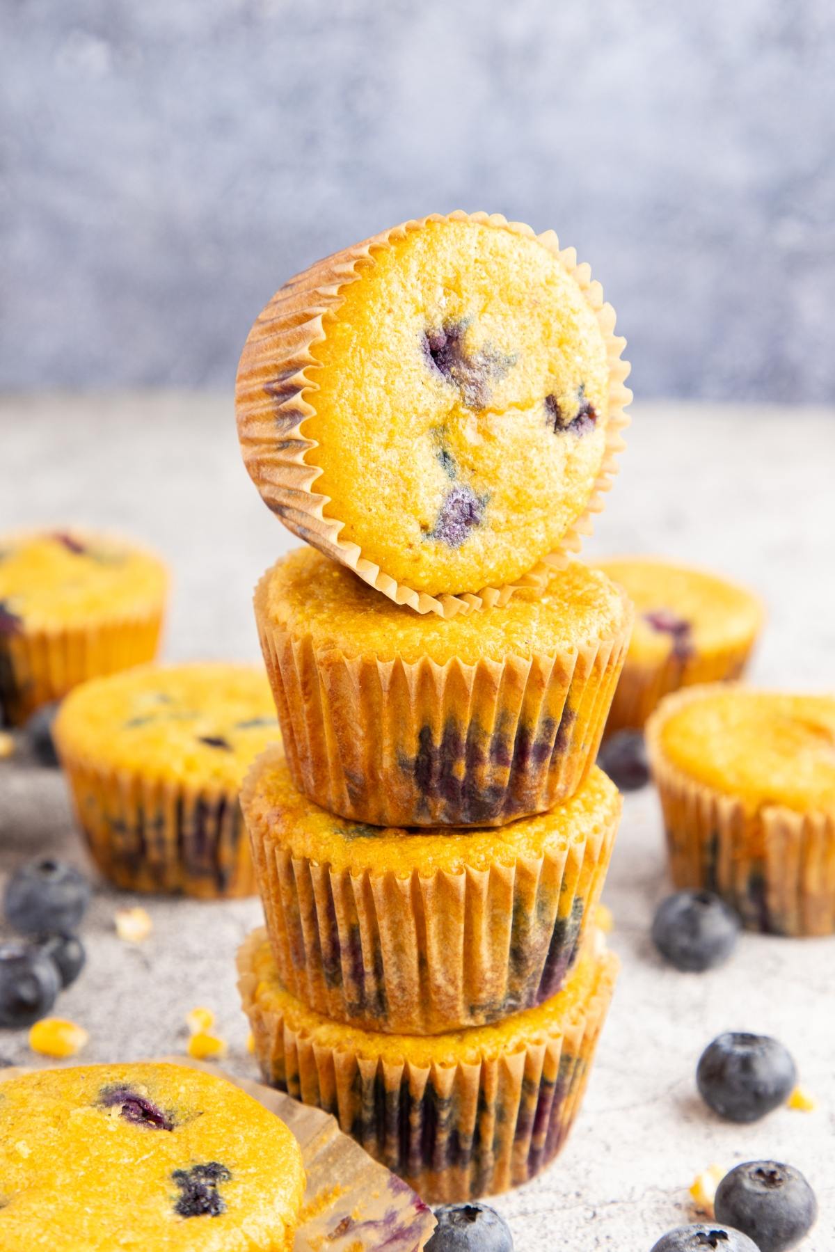 A stack of four blueberry muffins with scattered blueberries on a light surface.