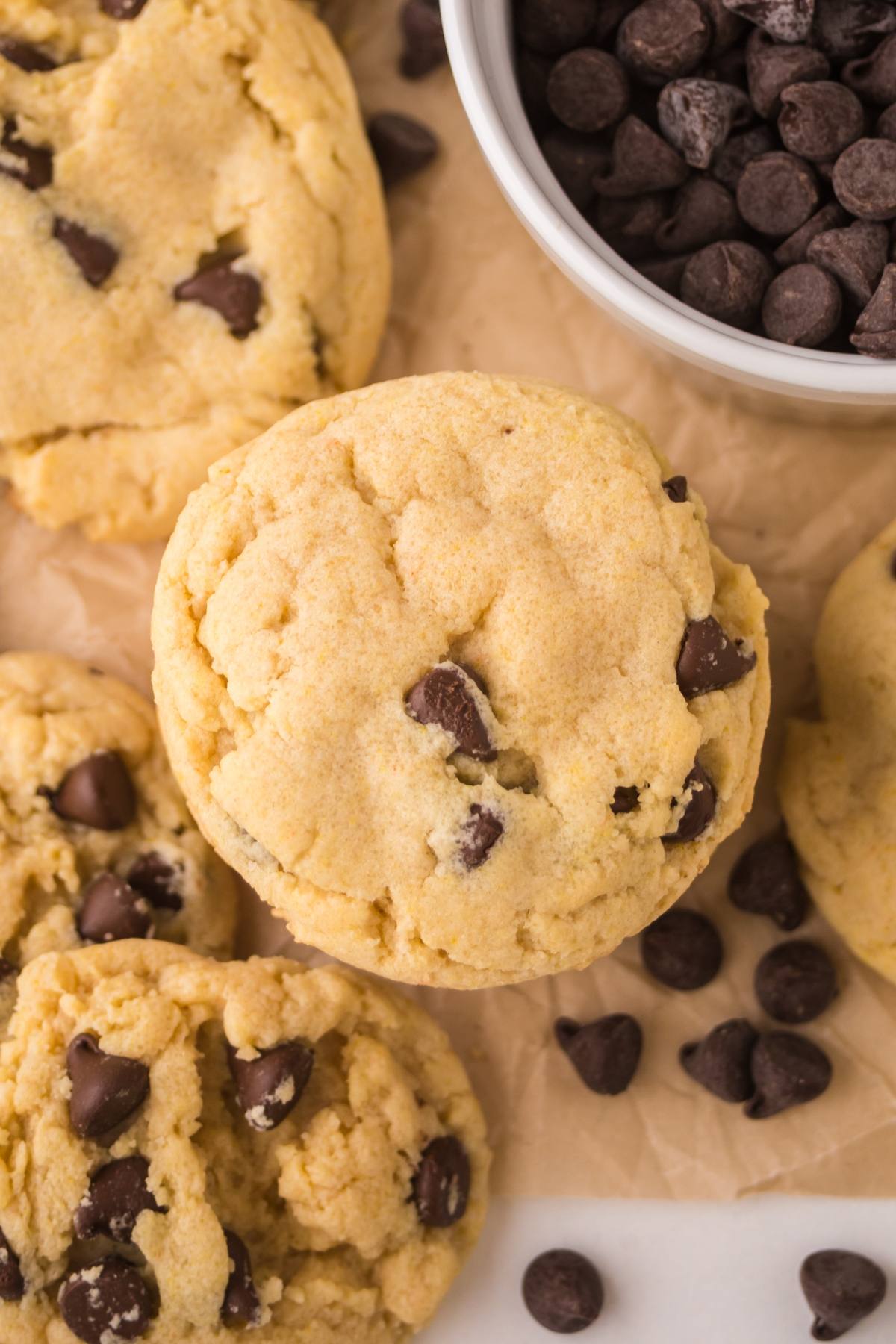 Close-up of chocolate chip cookies on parchment paper with a bowl of chocolate chips nearby.