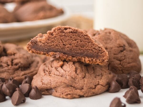 A stack of Chocolate Pudding Cookies with one split open, surrounded by chocolate chips.