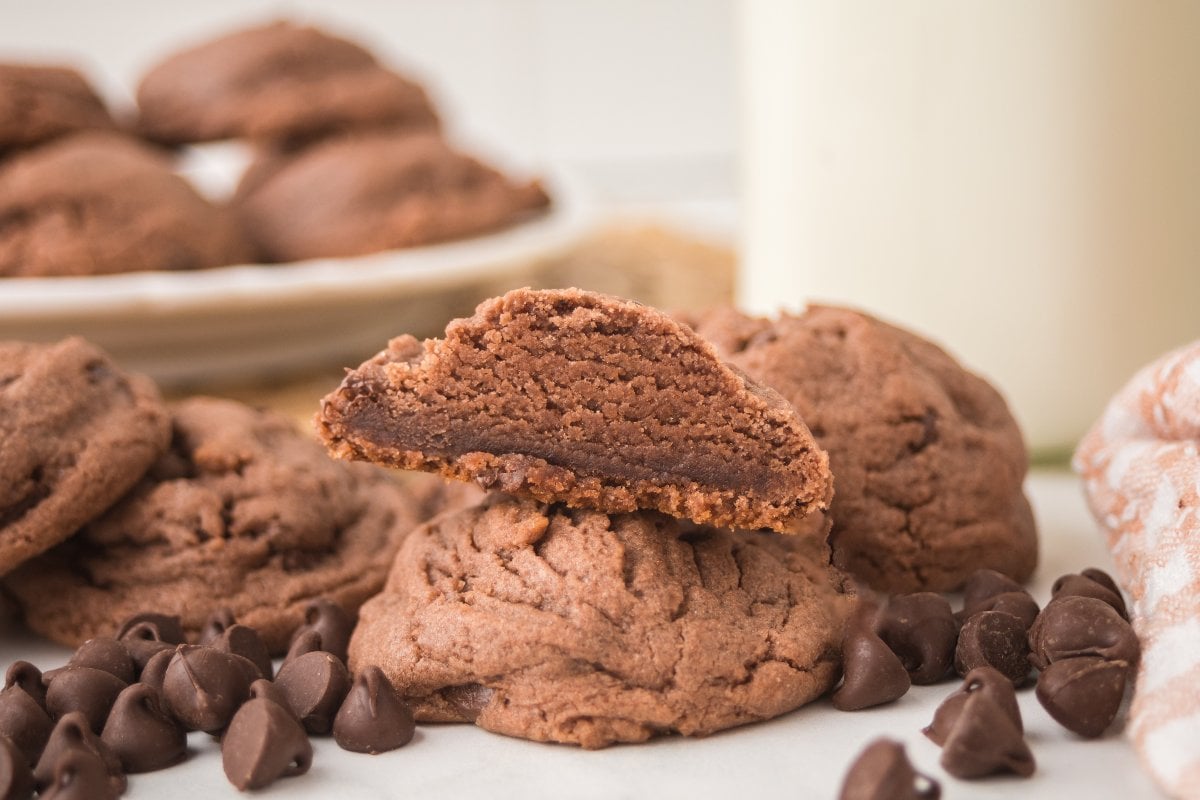 A stack of Chocolate Pudding Cookies, one split open, with gooey chocolate chips scattered around.