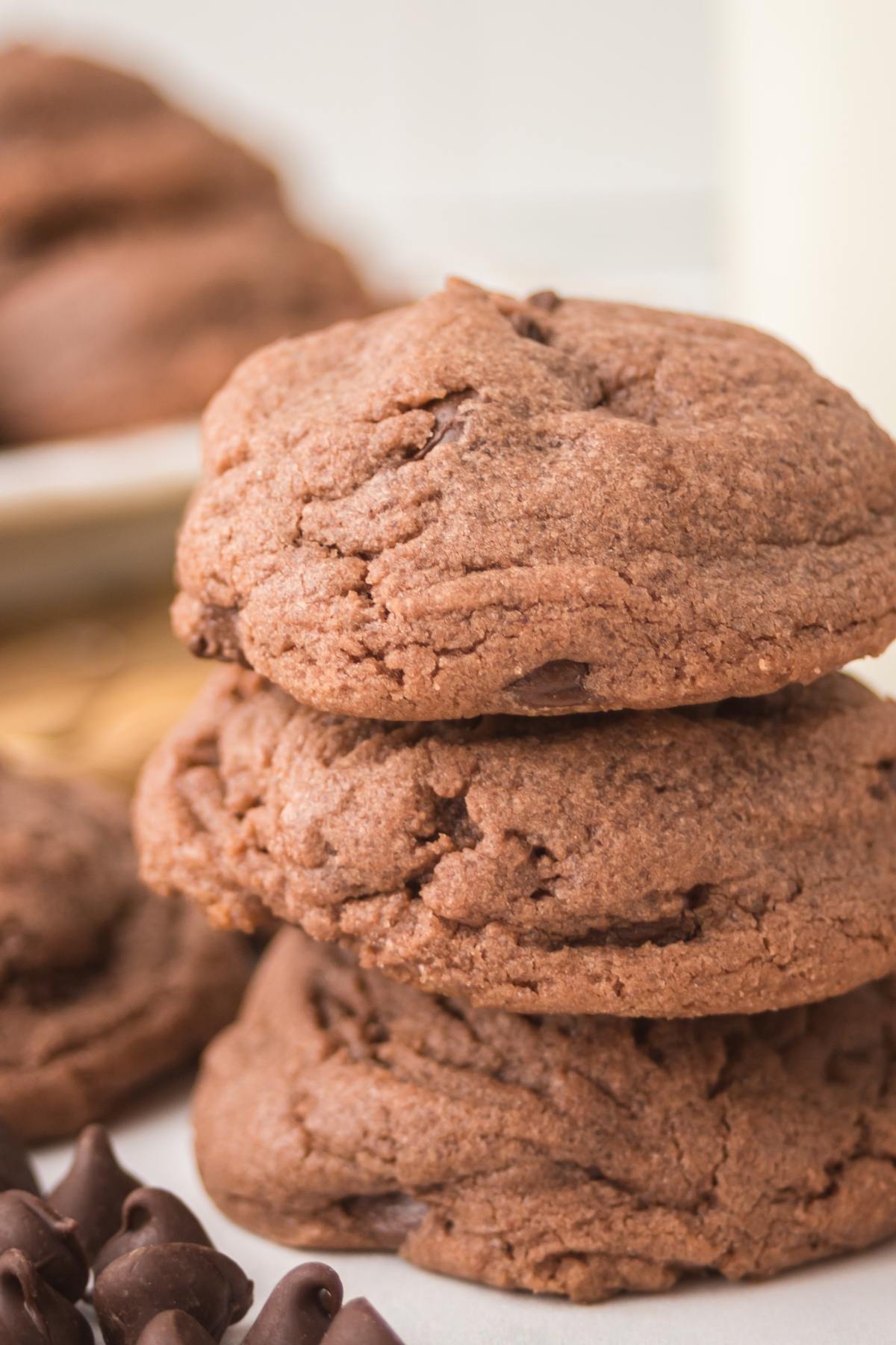 Three thick, chocolate cookies stacked on top of each other with chocolate chips nearby.