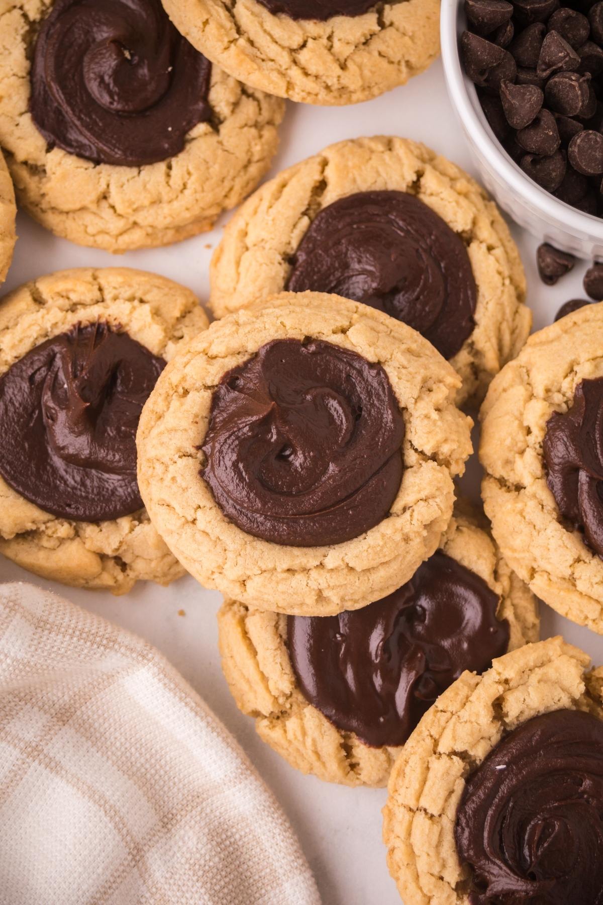 Thumbprint cookies topped with swirls of chocolate frosting, next to a bowl of chocolate chips.