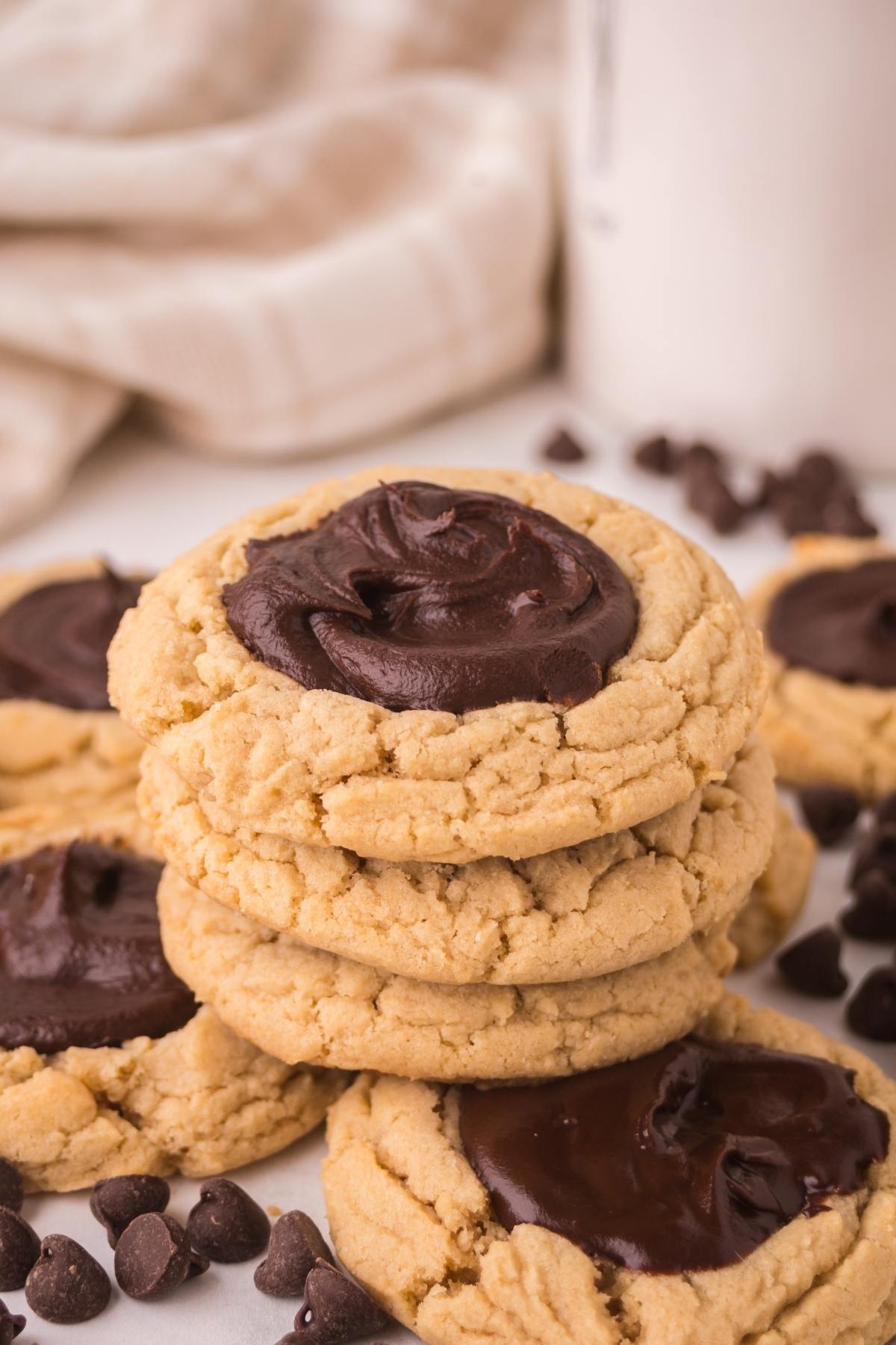 Stack of thumbprint cookies topped with chocolate fudge, surrounded by chocolate chips.