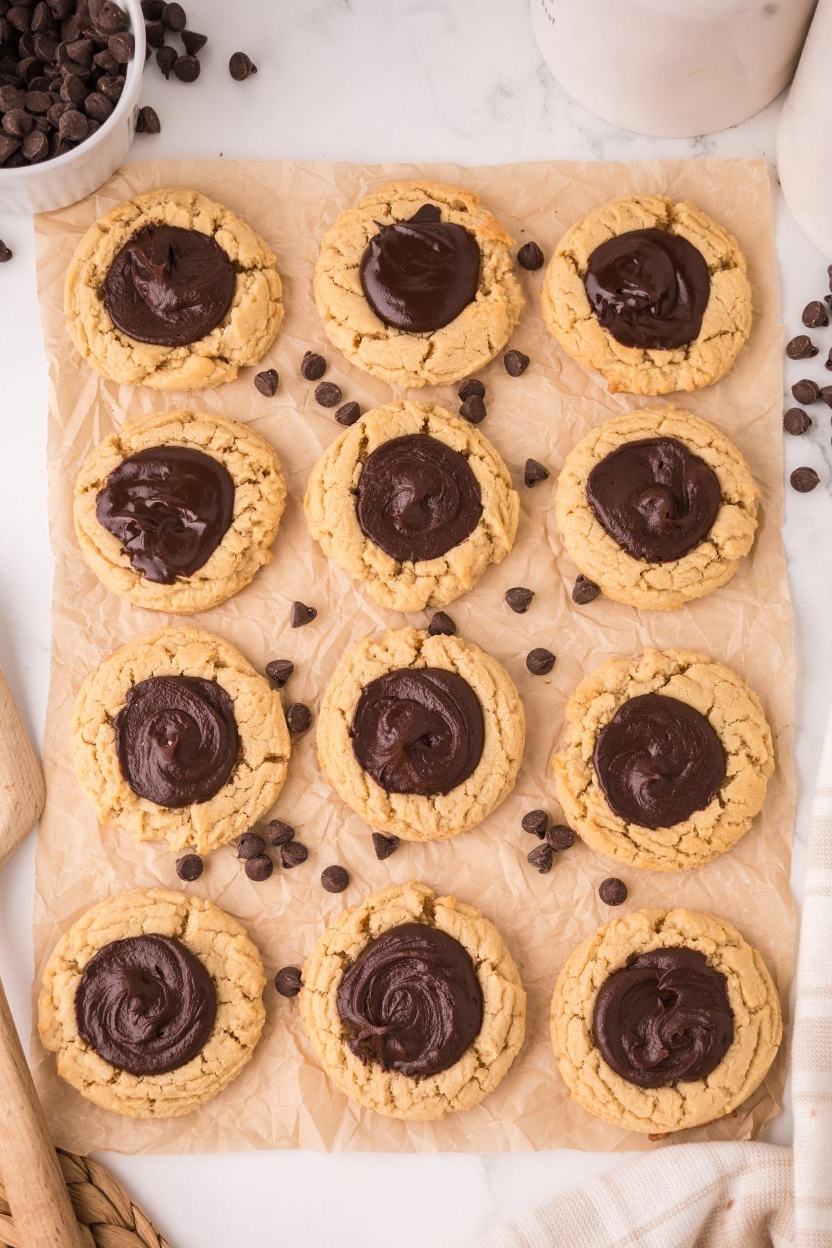 Twelve chocolate thumbprint cookies arranged on parchment paper, surrounded by chocolate chips.
