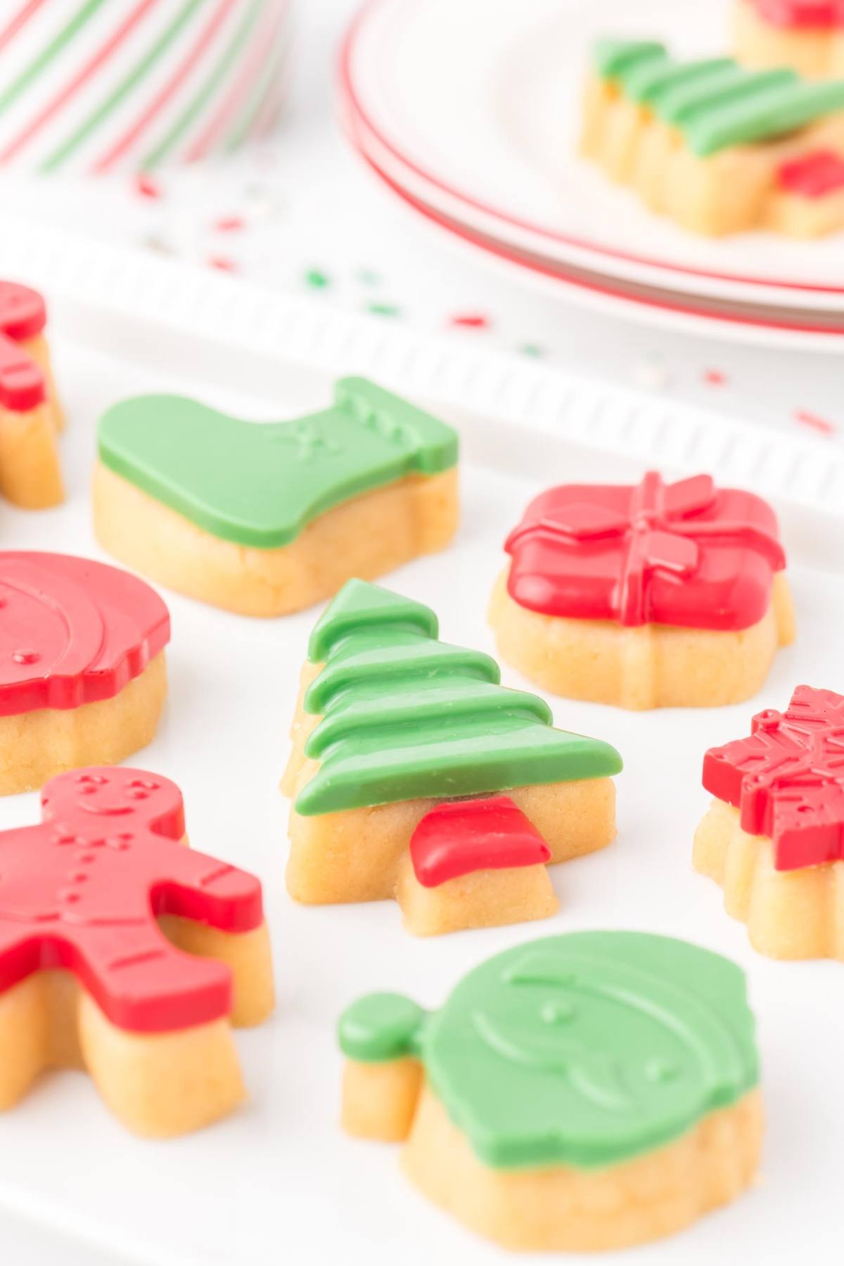 Christmas cookies decorated with green and red icing, shaped like trees, stockings, and gifts on a white tray.