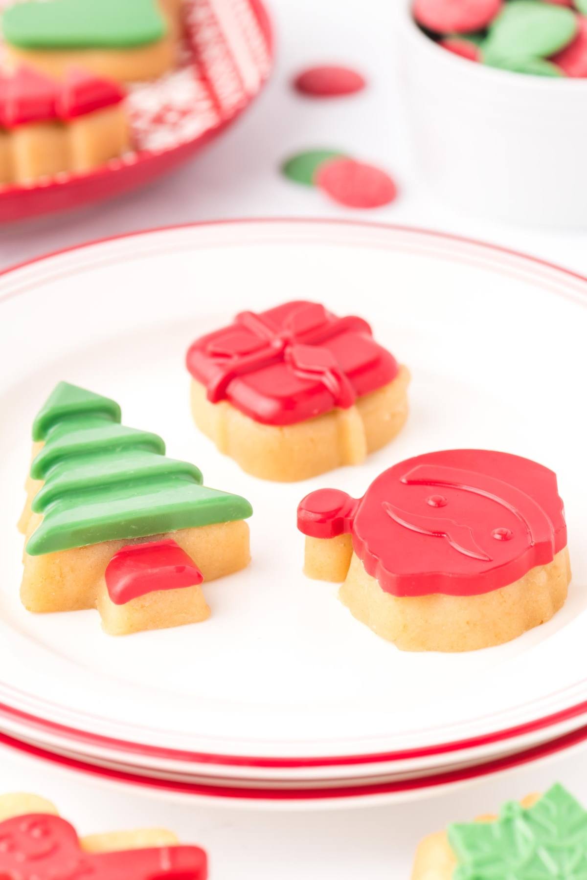 Christmas sugar cookies shaped like a tree, gift, and Santa, decorated with red and green icing on a plate.