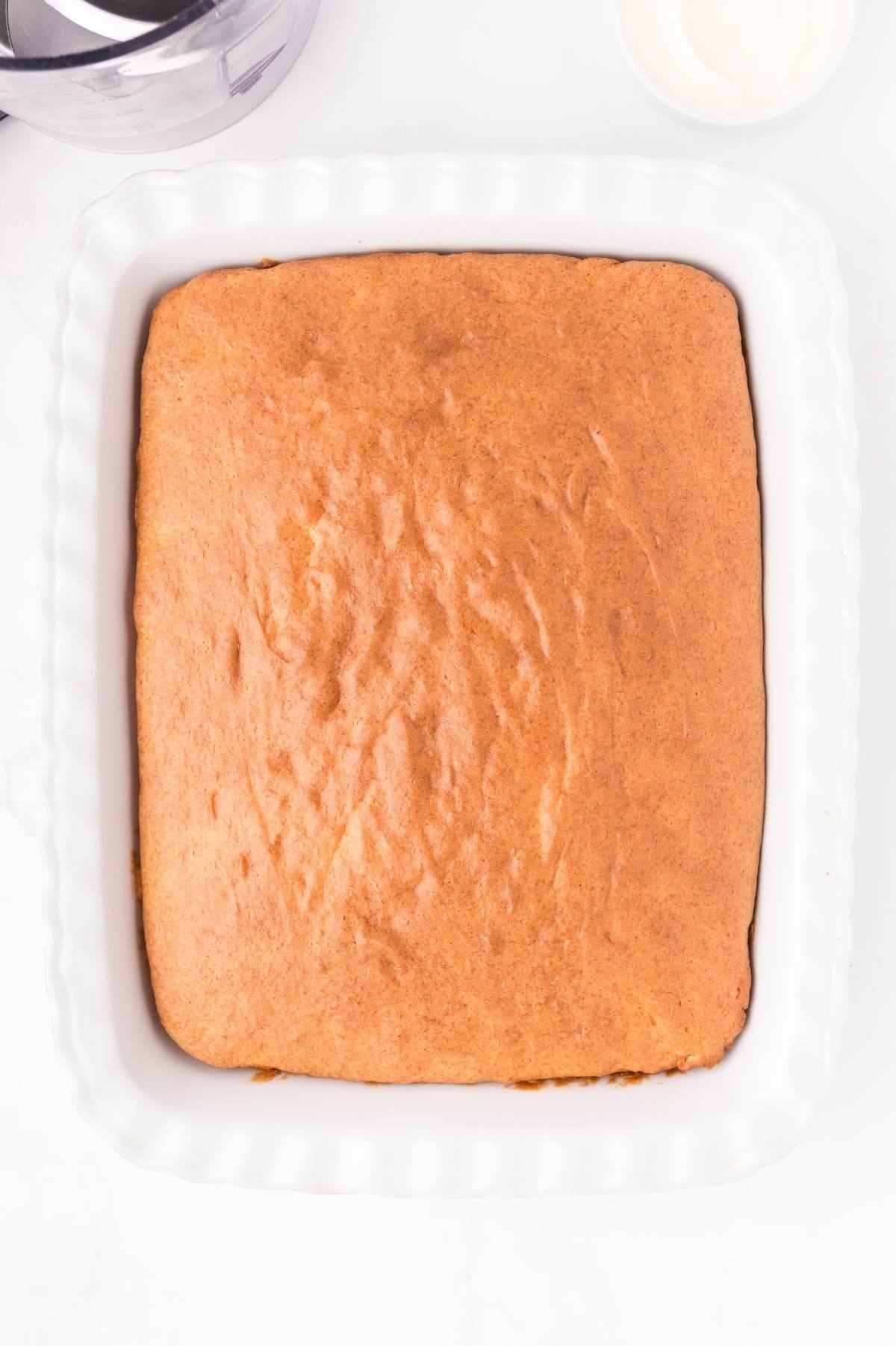 A golden-brown sheet cake in a white rectangular baking dish on a white surface.