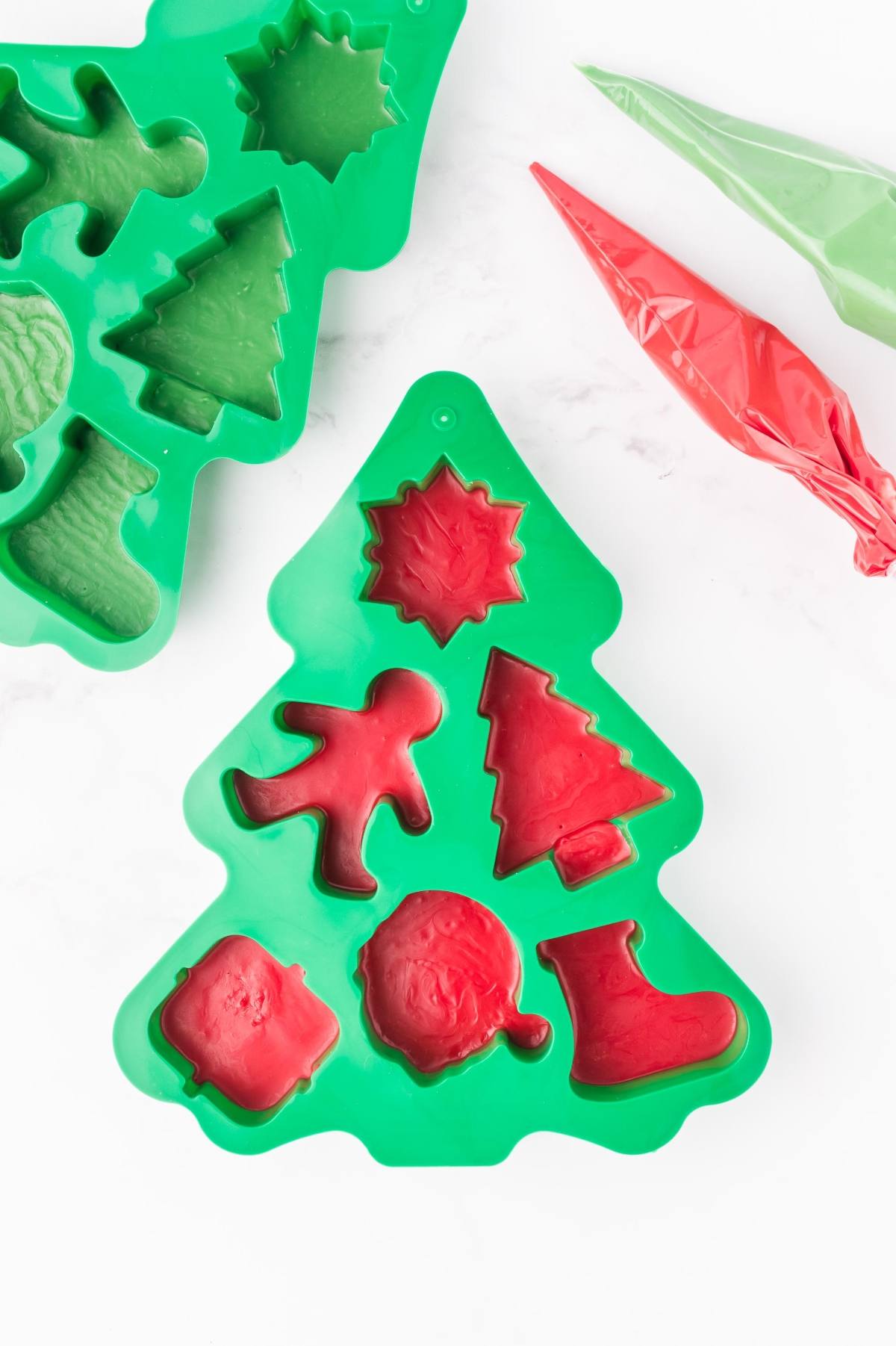 Green Christmas tree-shaped silicone mold with red holiday-themed treats and piping bags nearby.