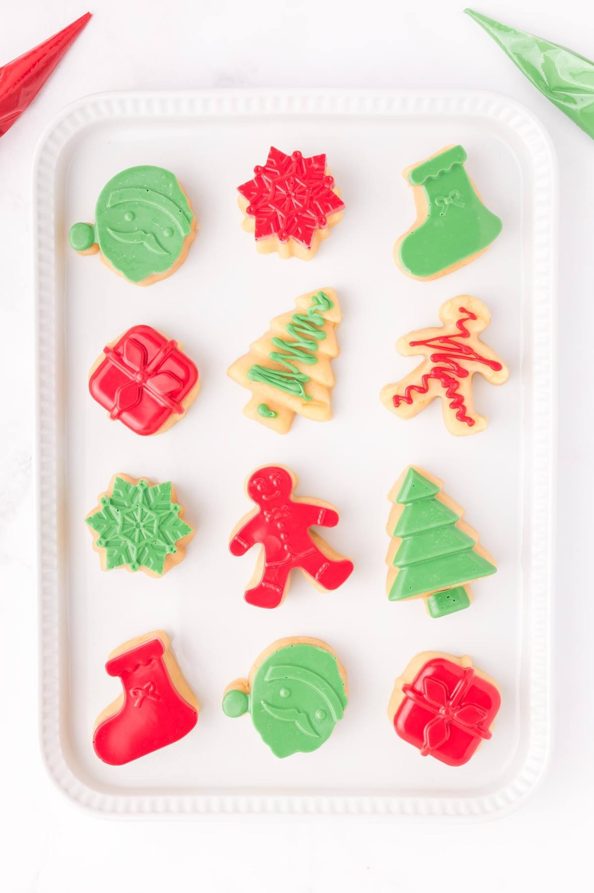 Iced Christmas cookies in festive shapes and colors arranged on a white rectangular tray.