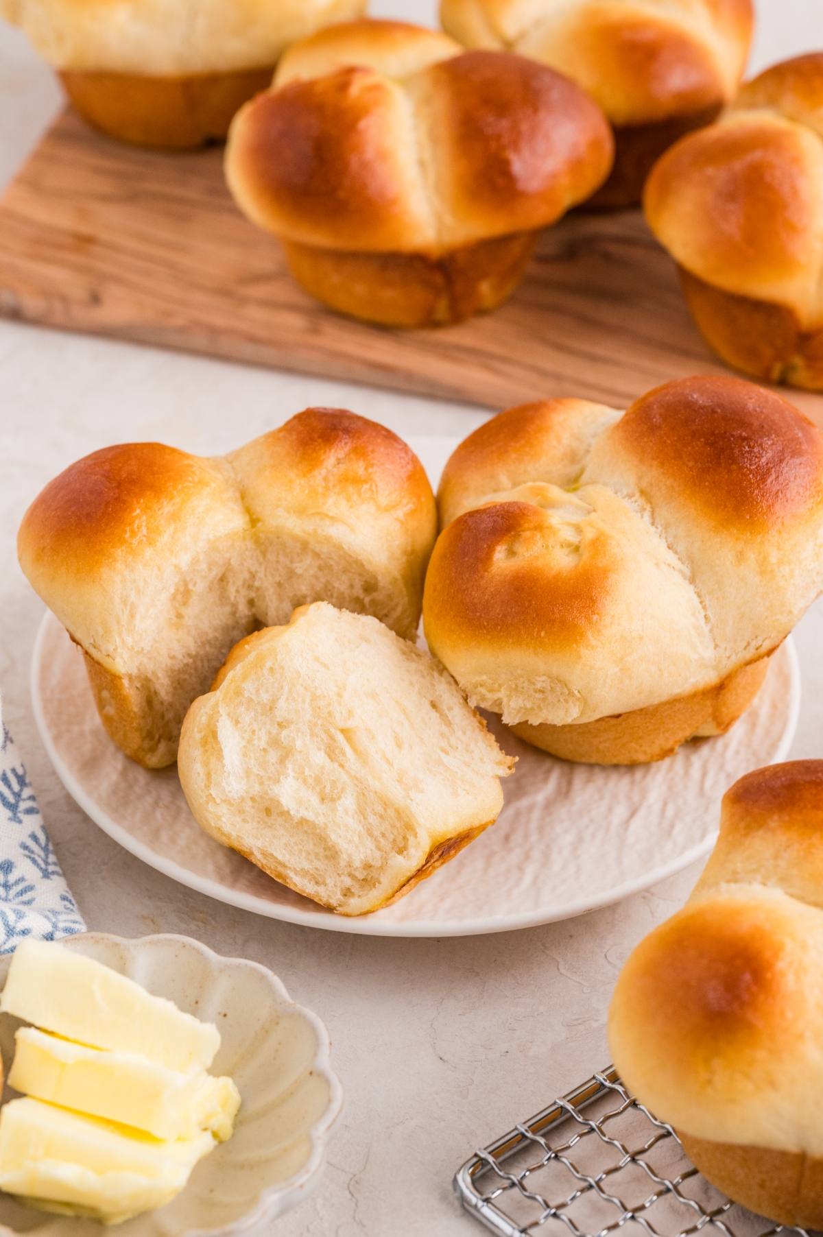 Golden brown cloverleaf rolls on a plate, with one roll split open, and a dish of butter nearby.