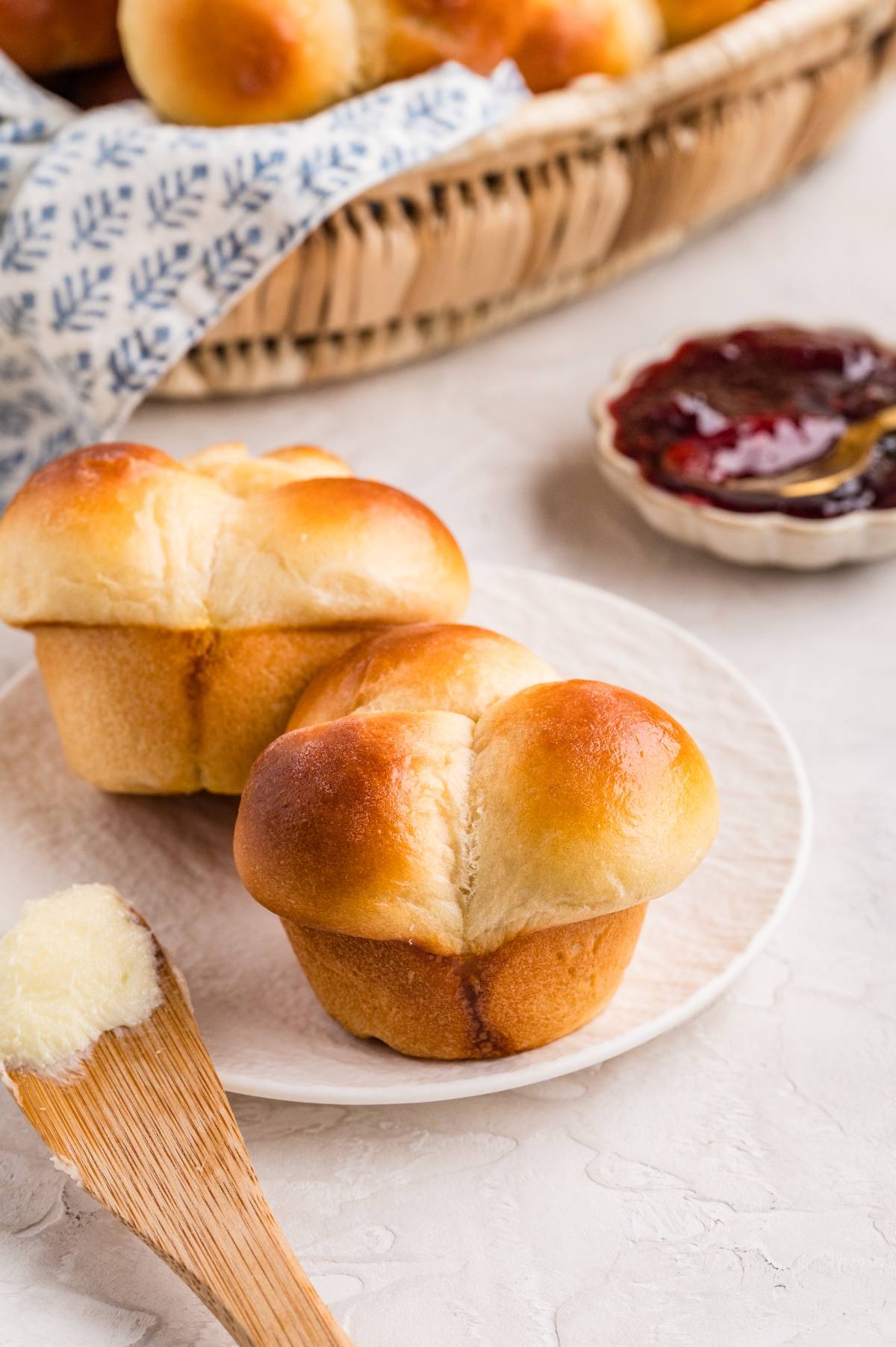Two golden brown rolls on a plate, with a dish of jam and a wooden butter spreader nearby.