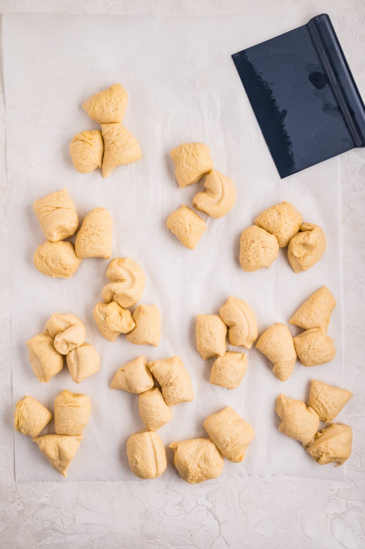 Chunks of dough scattered on parchment paper next to a dark blue dough scraper.
