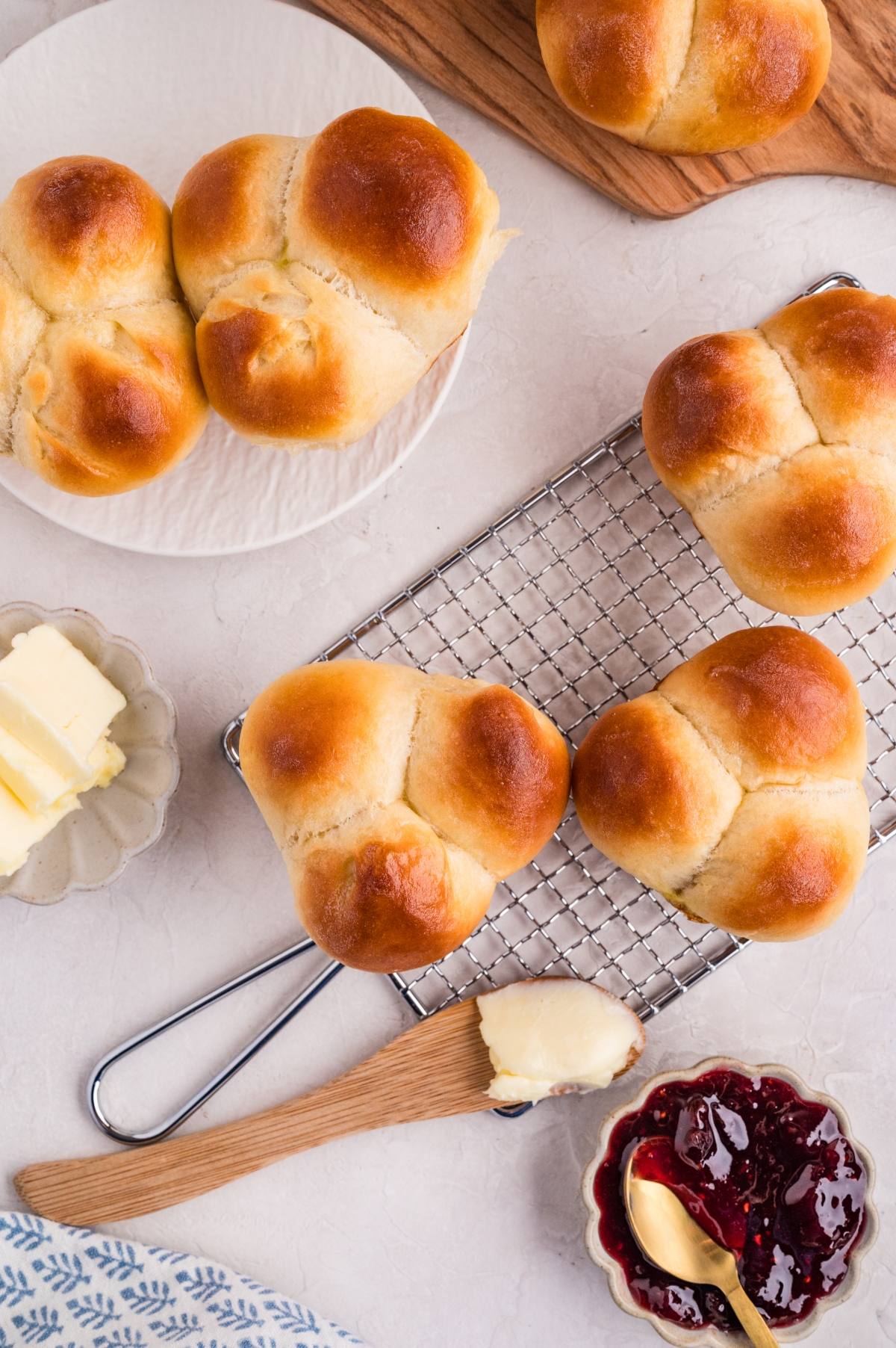 Golden cloverleaf rolls on a cooling rack with butter and jam on the side.