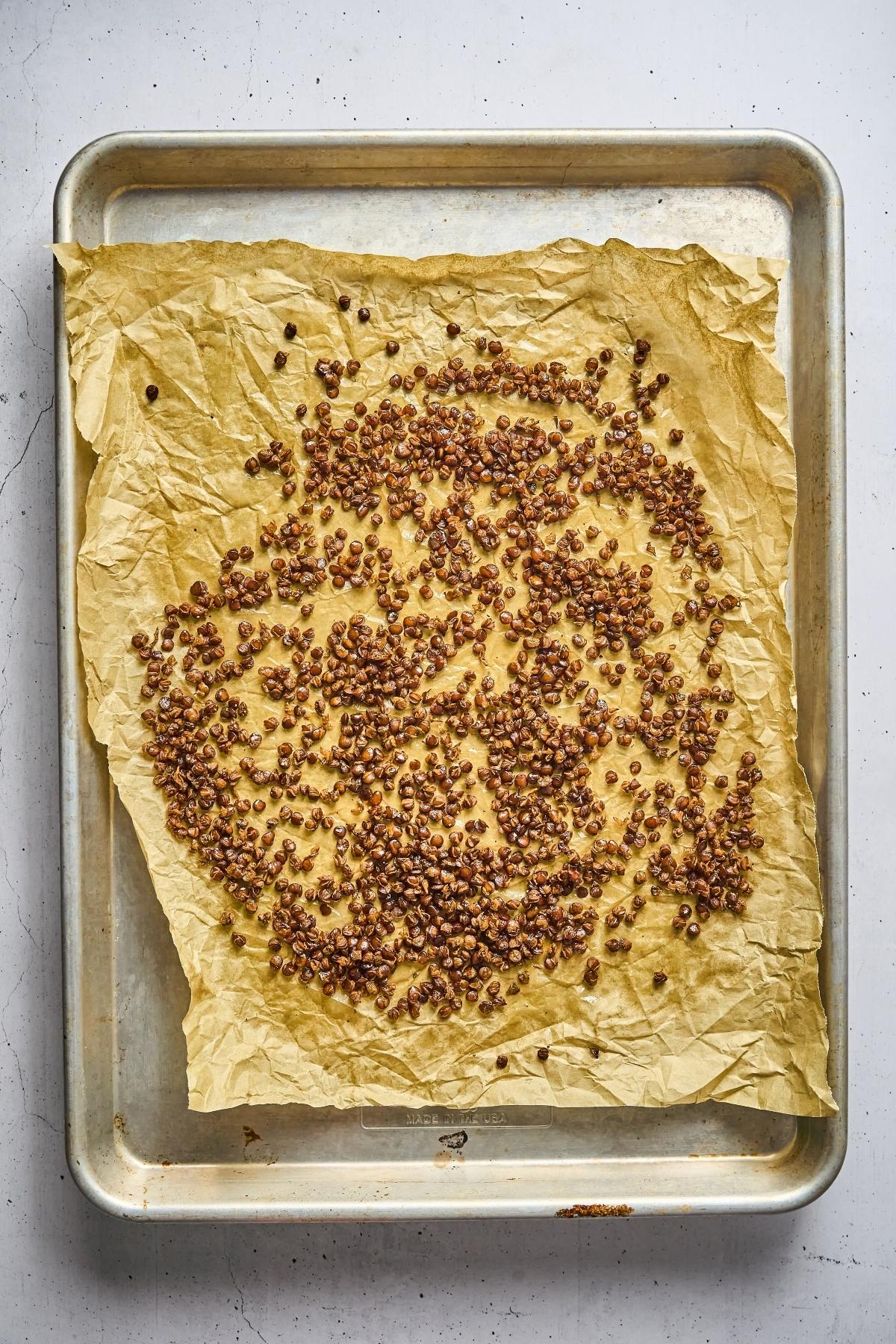 Toasted buckwheat groats spread on parchment paper over a baking sheet.