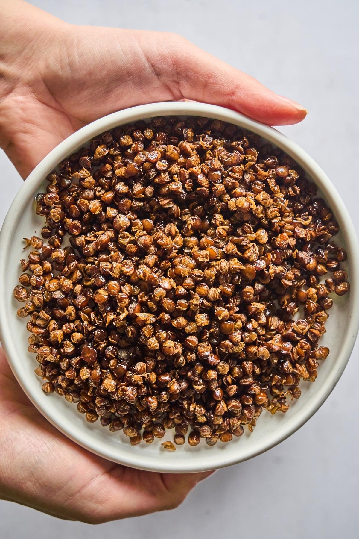 A bowl of roasted buckwheat groats held in two hands over a light background.