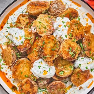 Crispy Parmesan Potatoes topped with creamy herb sauce and chopped parsley on a white plate.