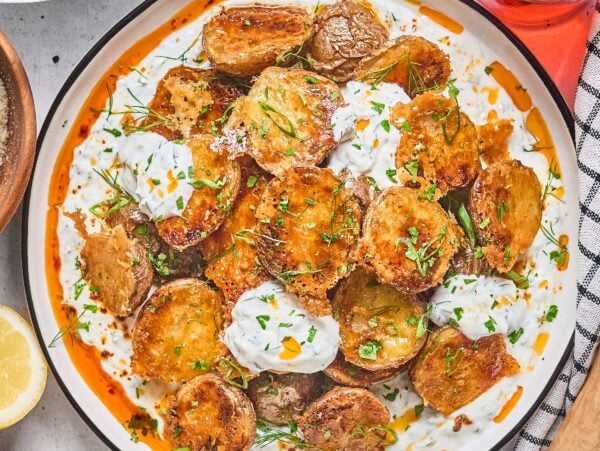 Crispy Parmesan Potatoes topped with creamy herb sauce and chopped parsley on a white plate.