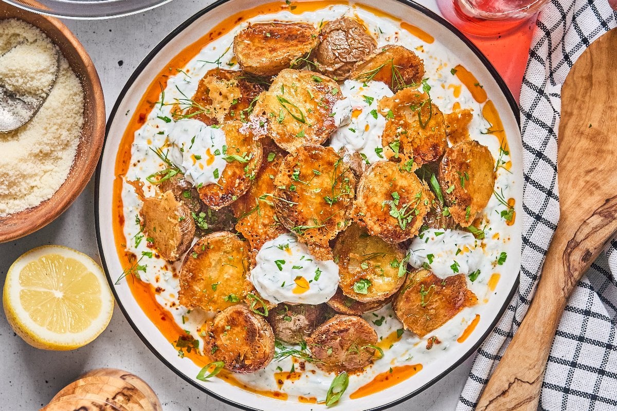 Crispy Parmesan Potatoes on a plate with creamy sauce, fresh herbs, and a drizzle of orange oil.