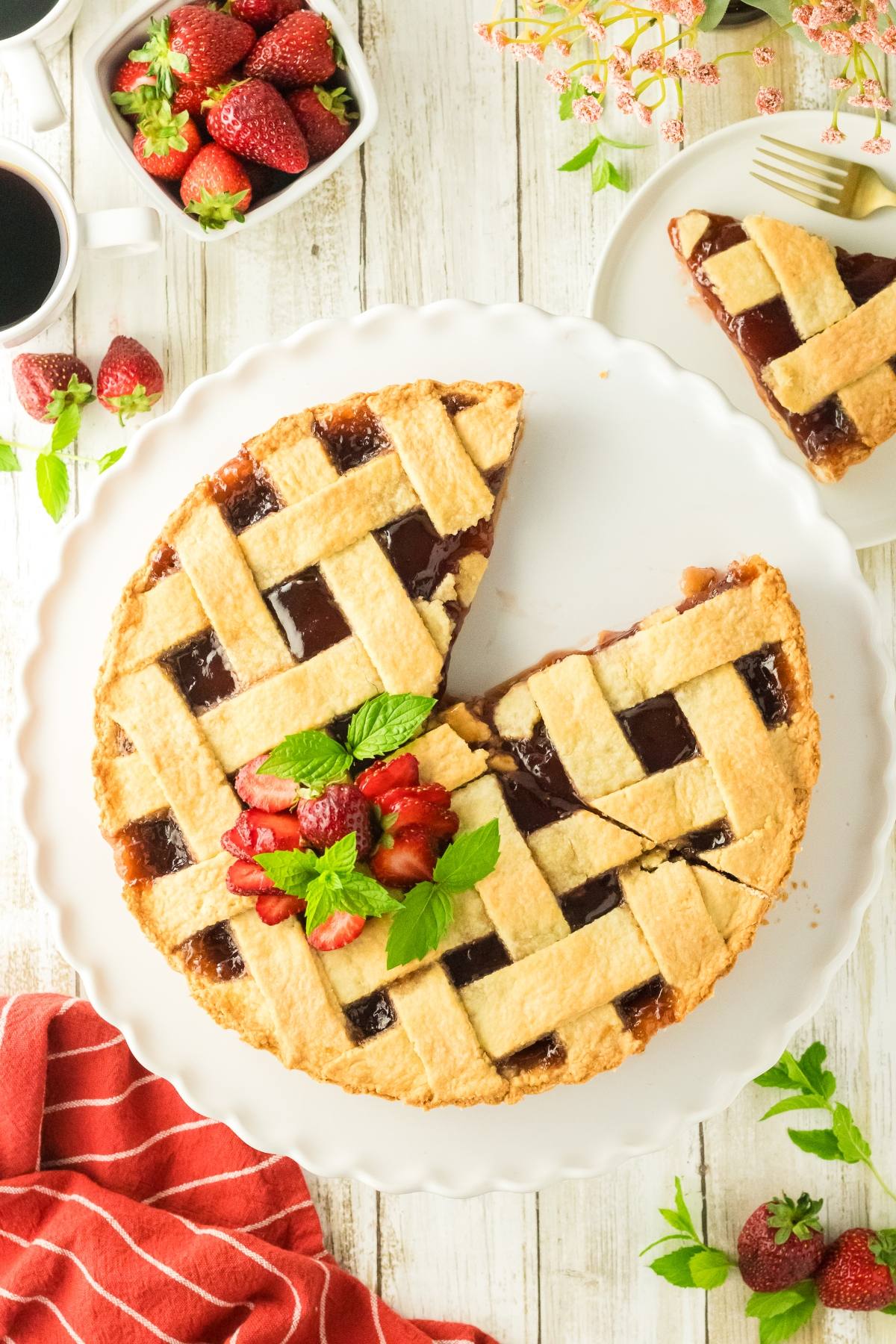 A lattice-topped strawberry pie with a slice missing, garnished with fresh strawberries and mint.